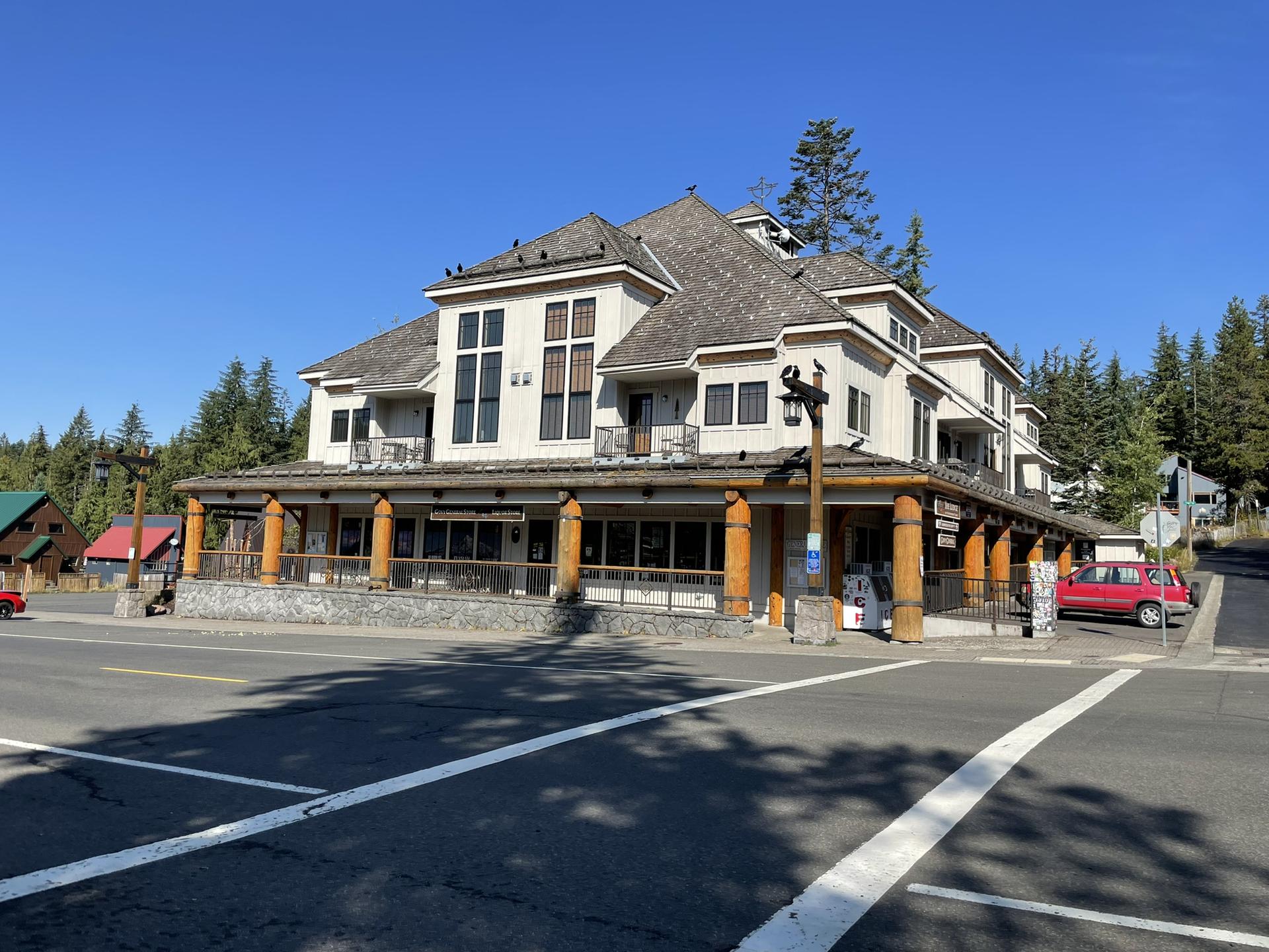 Large lodge-style building with a porch, surrounded by evergreen trees under clear blue sky.