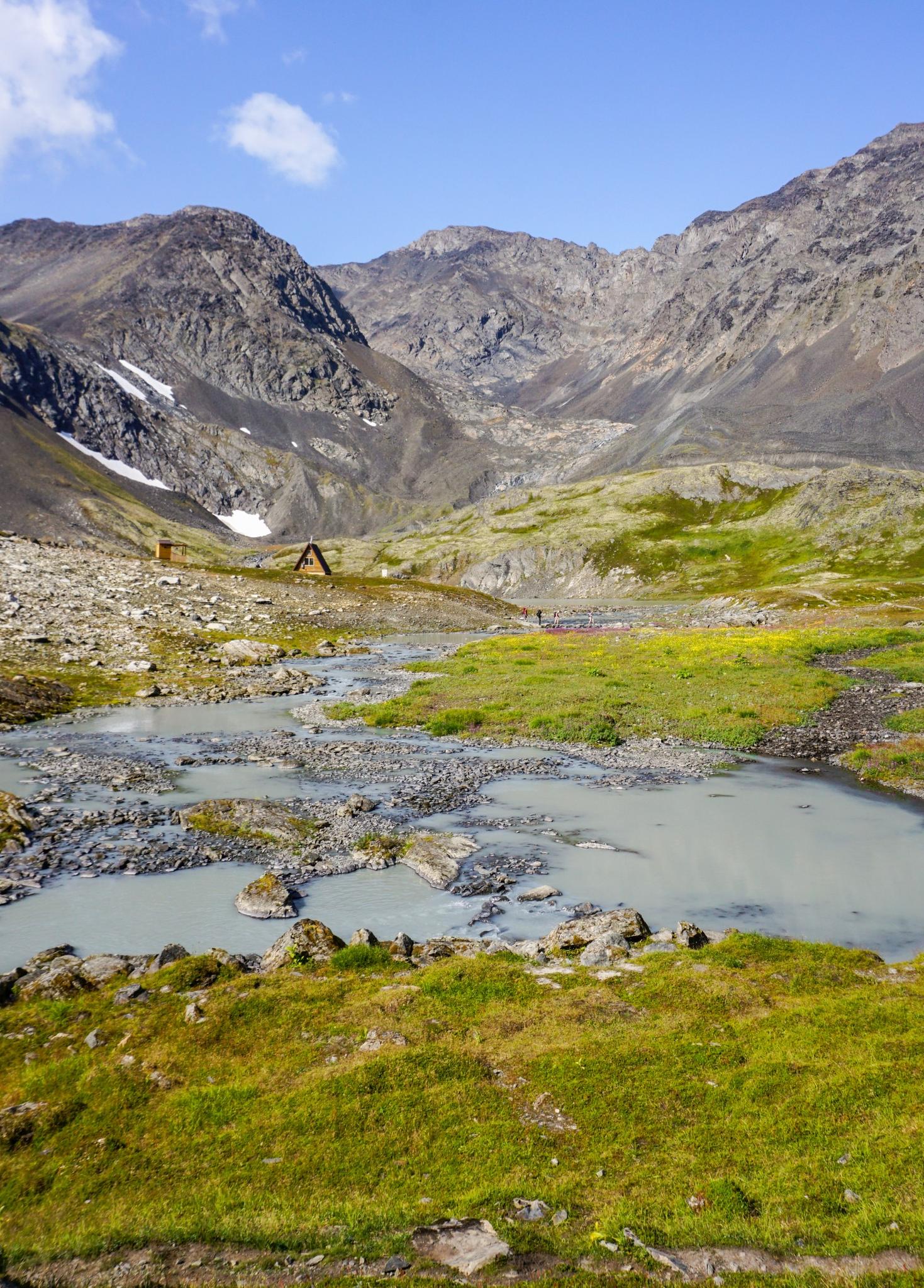 Rocky stream flowing through a mountain landscape with a small cabin.