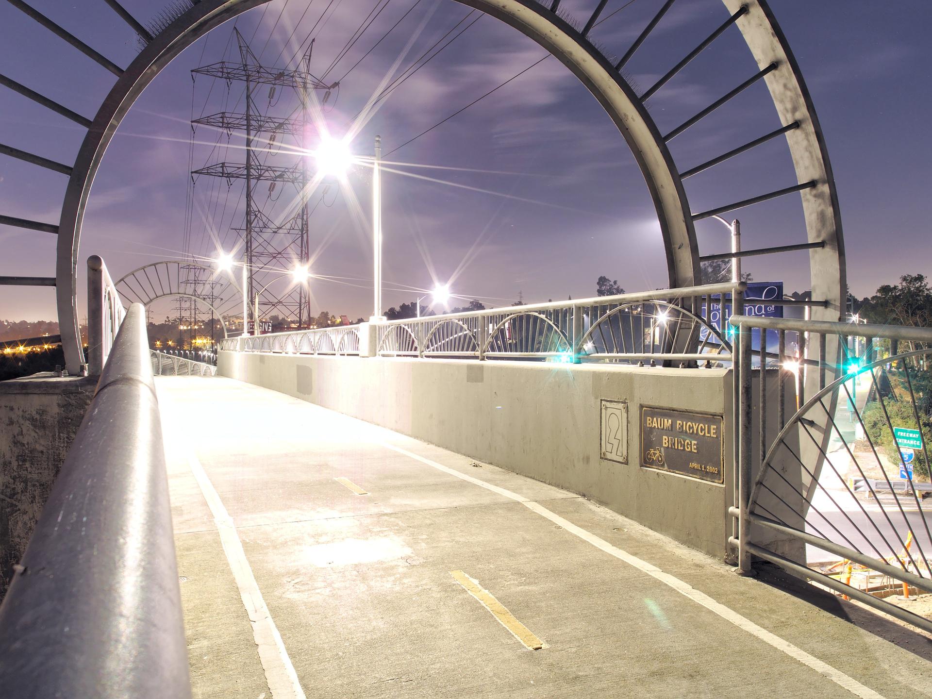 Arched pedestrian bridge illuminated by bright streetlights at night.