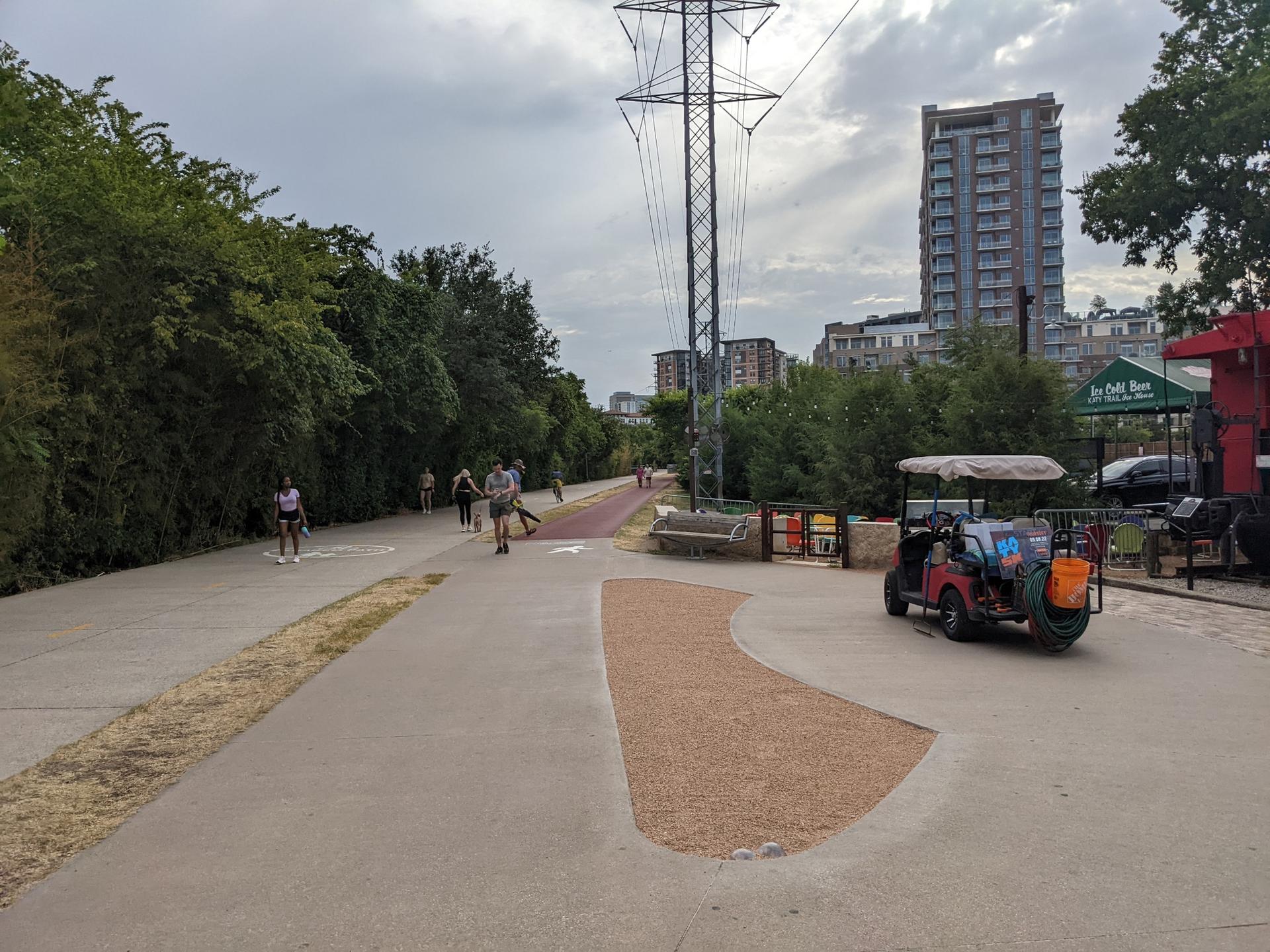 People walk and ride on a paved path under power lines, urban background.