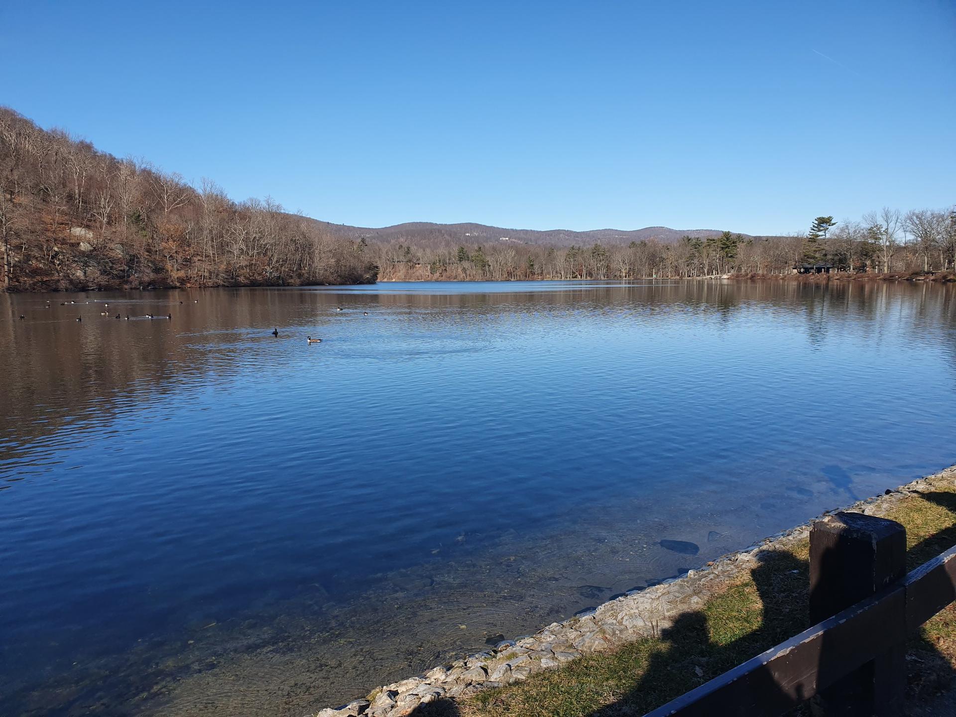 Serene lake reflecting a clear blue sky, bordered by wooded hills.