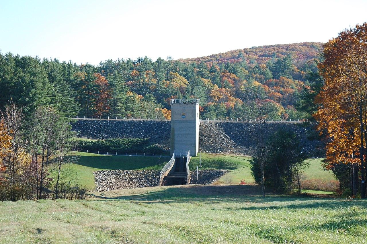 A large concrete dam with stairs, surrounded by autumn trees and green grass.