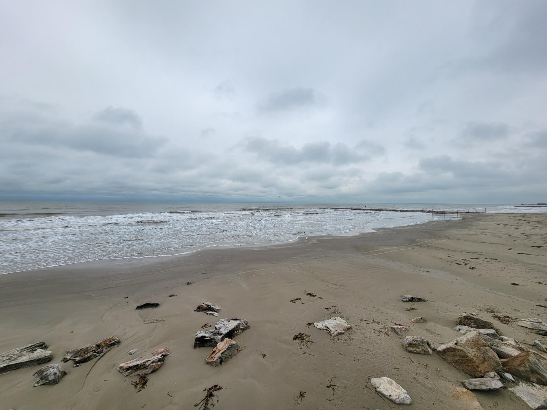 Wide sandy beach with ocean waves under a cloudy, overcast sky.