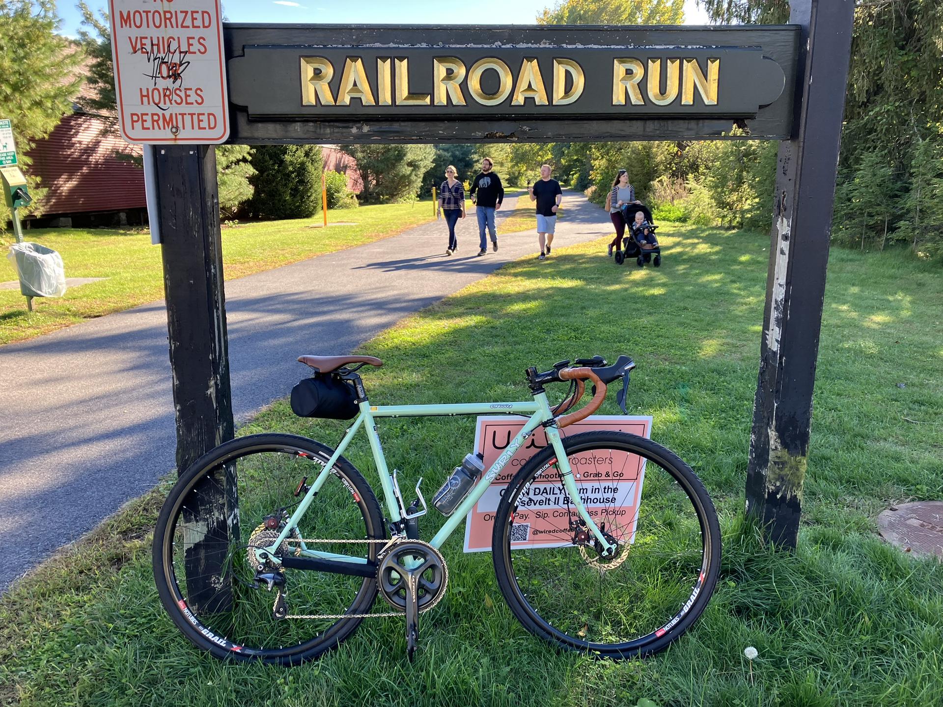 A light green bicycle parked next to a sign, with people walking behind.
