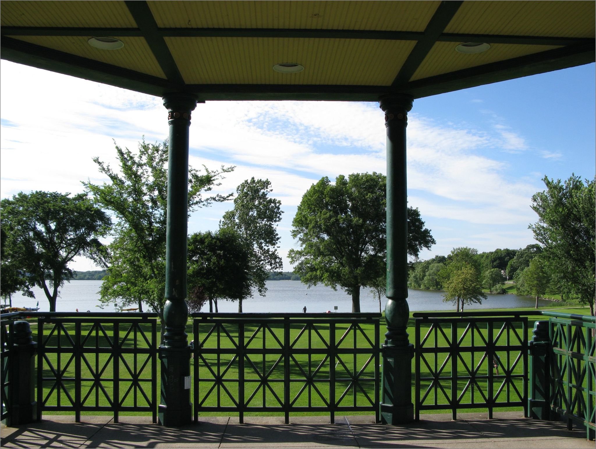 View from a green gazebo overlooking a lake with lush trees on a sunny day. - Lake Quannapowitt Trail