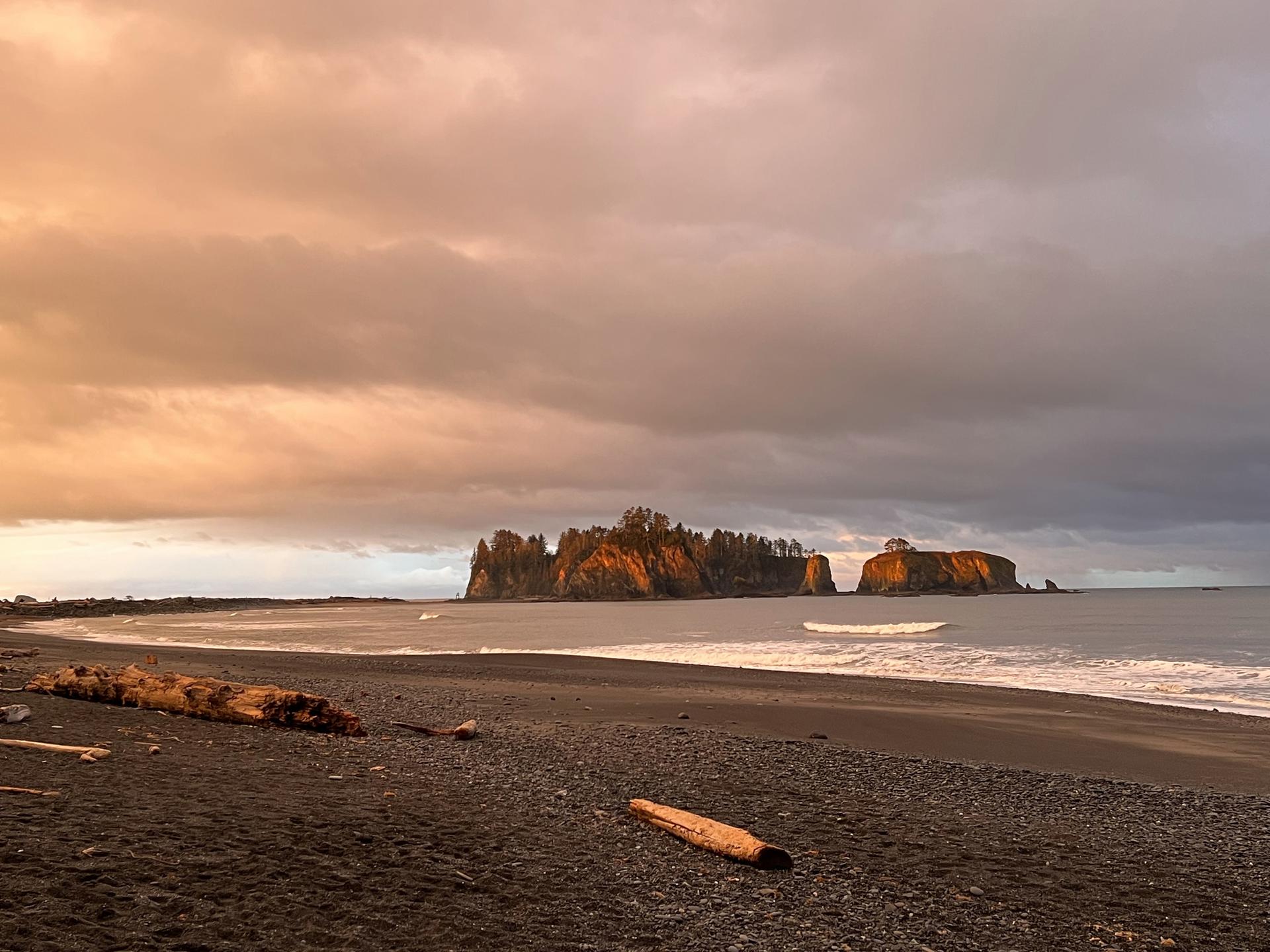 Dramatic sunset over a rocky beach with sea stacks and driftwood.