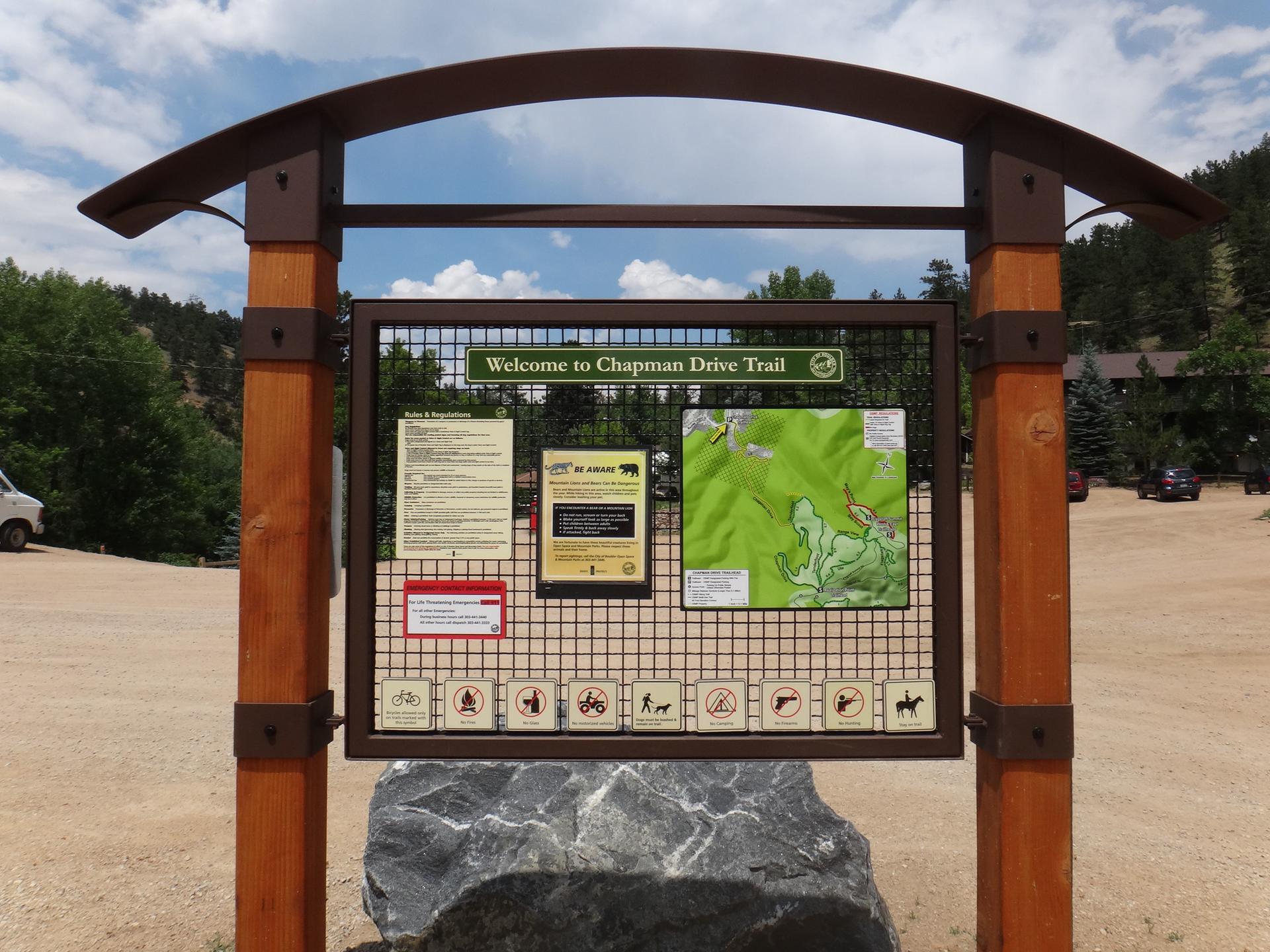 An outdoor information kiosk with maps and rules under a partly cloudy sky.