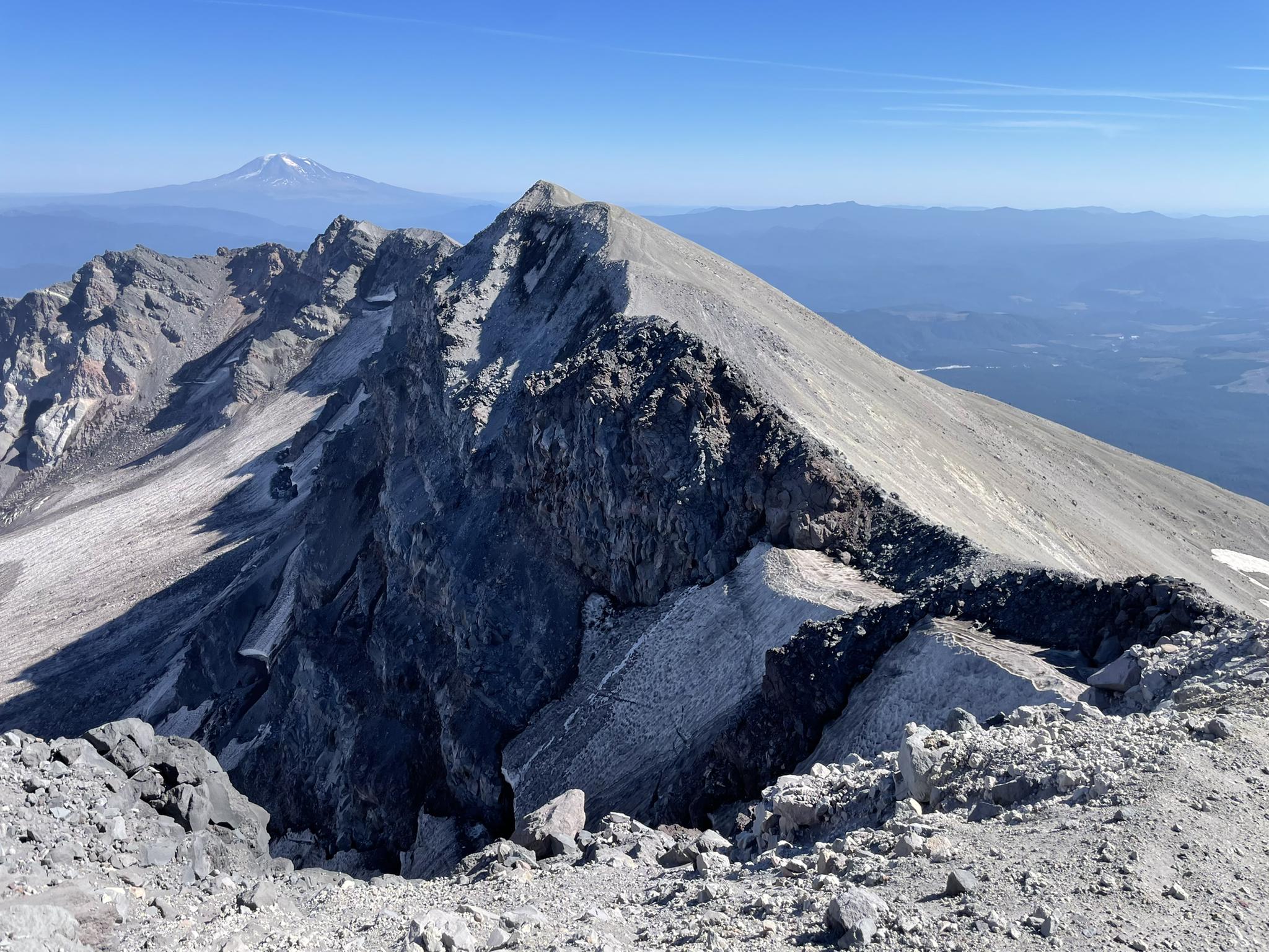 Sharp, rocky mountain ridge with a distant snow-capped peak under clear sky.