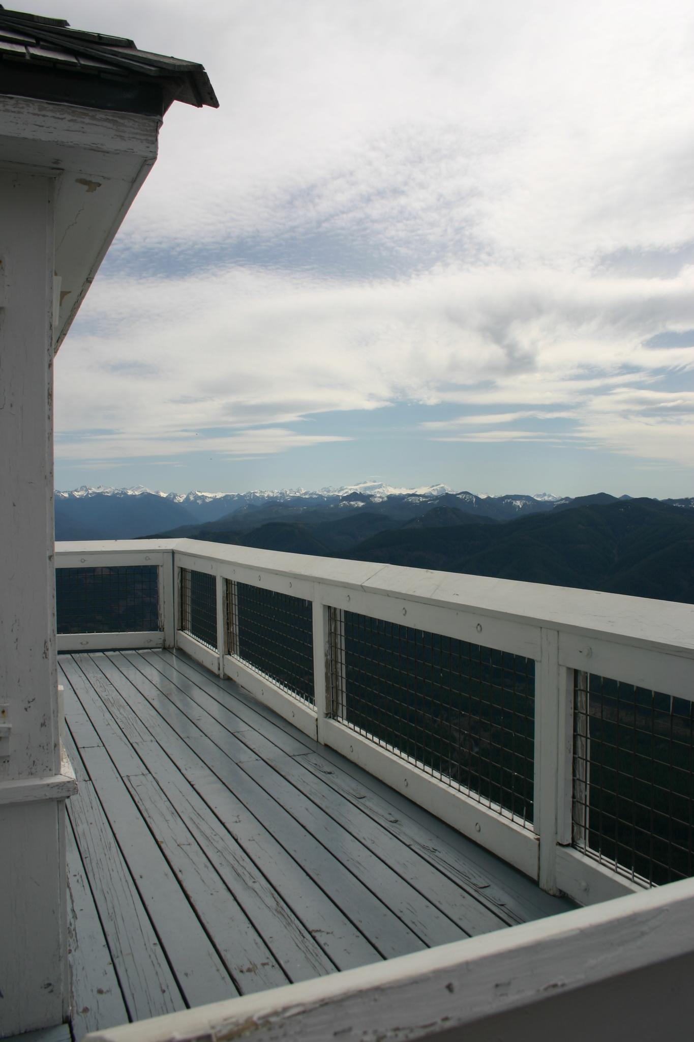 Wooden deck of a building overlooking distant mountains under a cloudy sky.