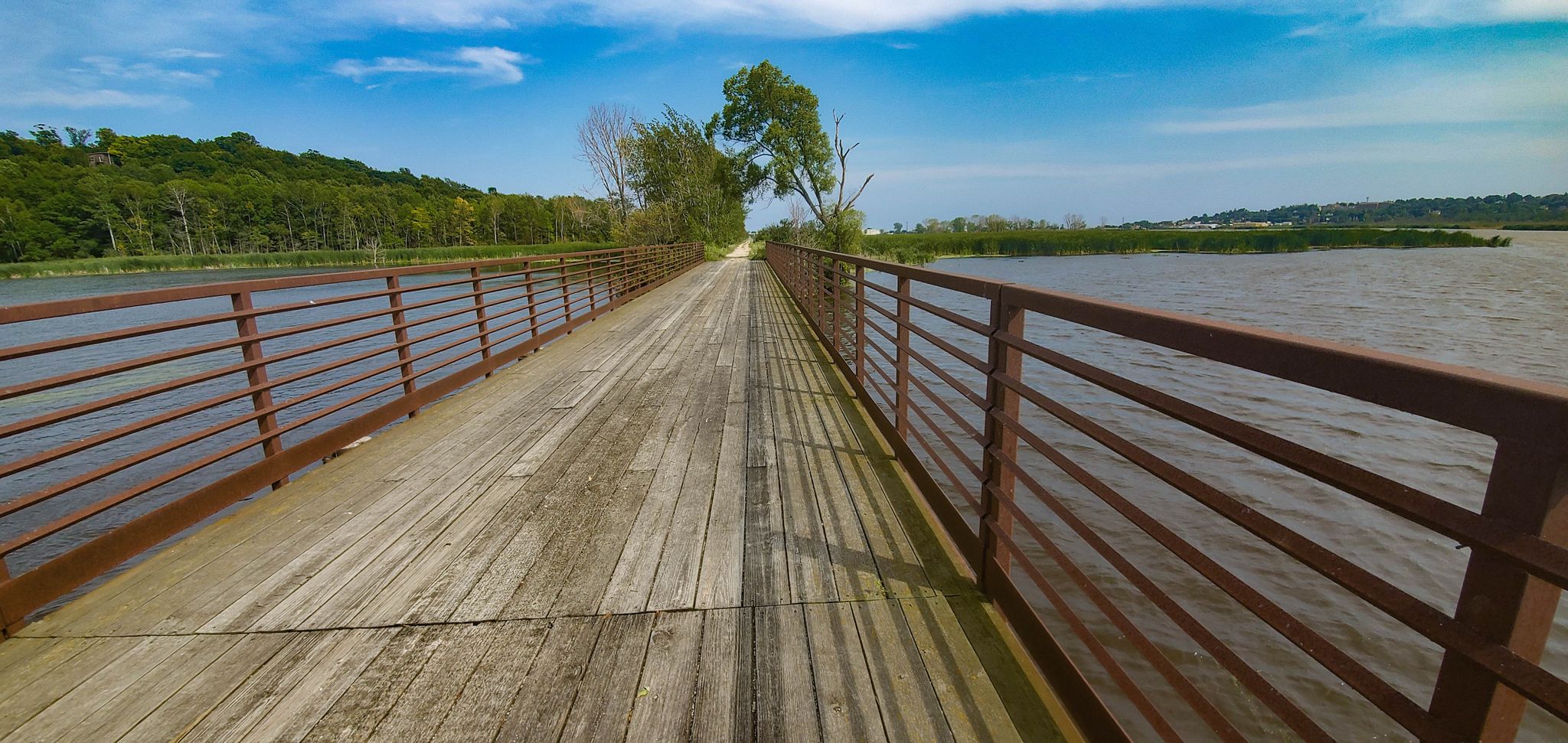 Sunny wooden bridge over water with railings and distant green hills. - Ahnapee State Trail