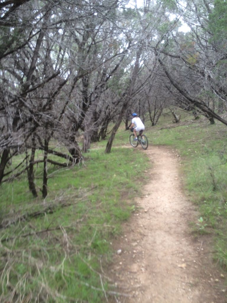 Person mountain biking on a winding dirt path through a dense, wooded area. - Great Escape Trail