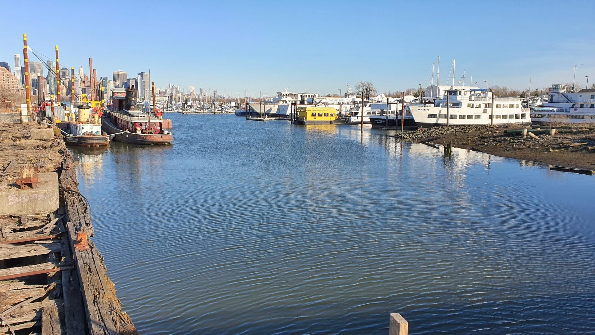 A sunny waterway with many boats docked along industrial shores.