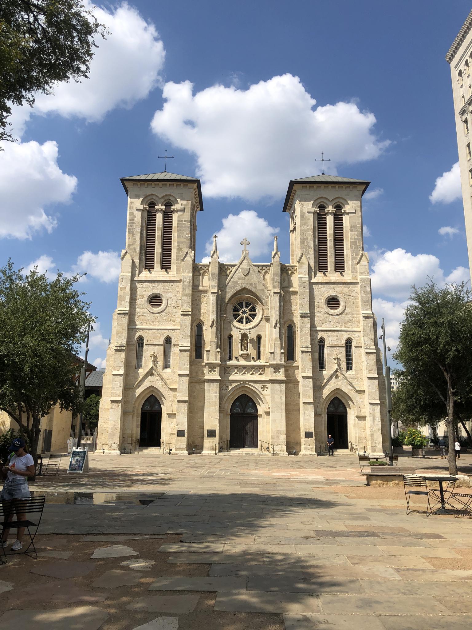 Grand stone church with twin towers and a plaza under a cloudy blue sky.