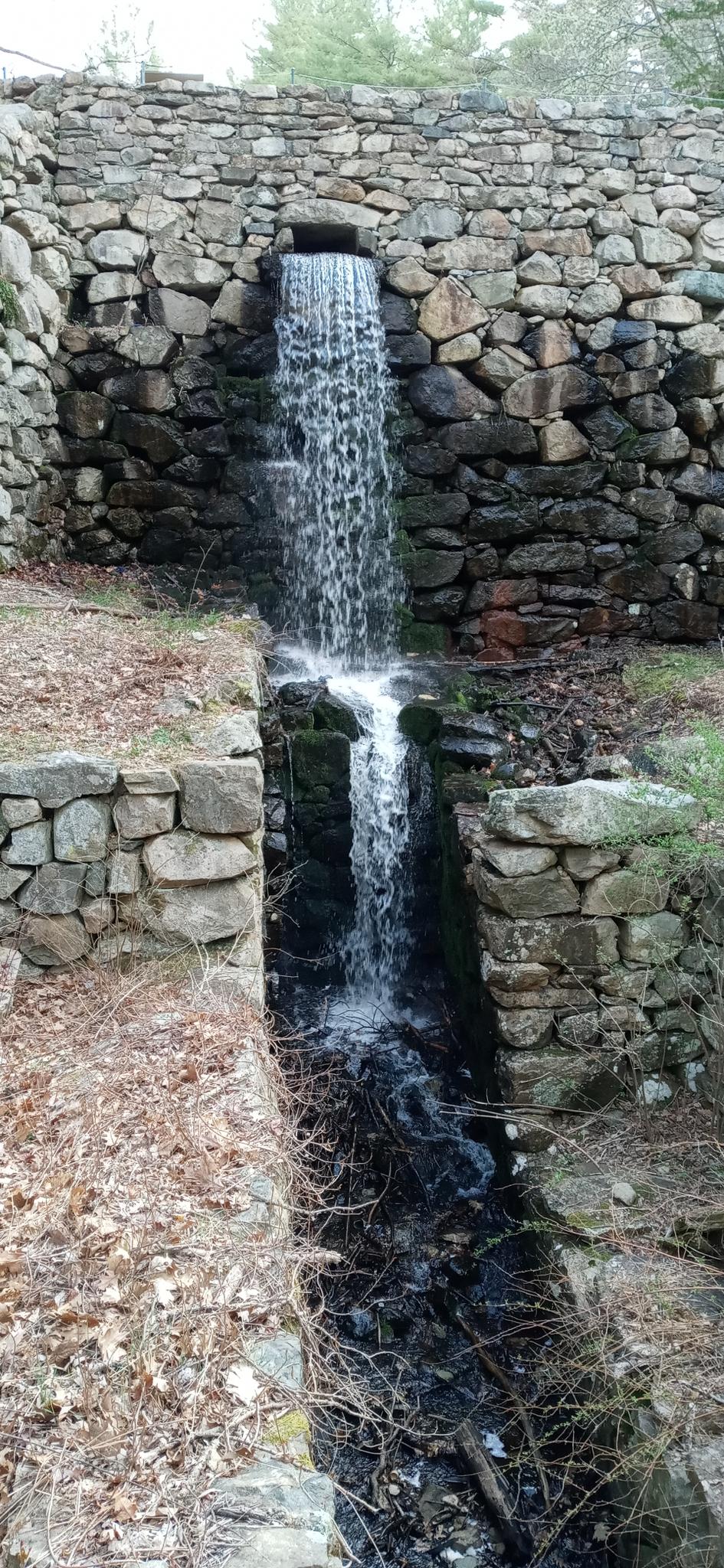 Waterfall cascading over a tall stone wall into a dark channel.