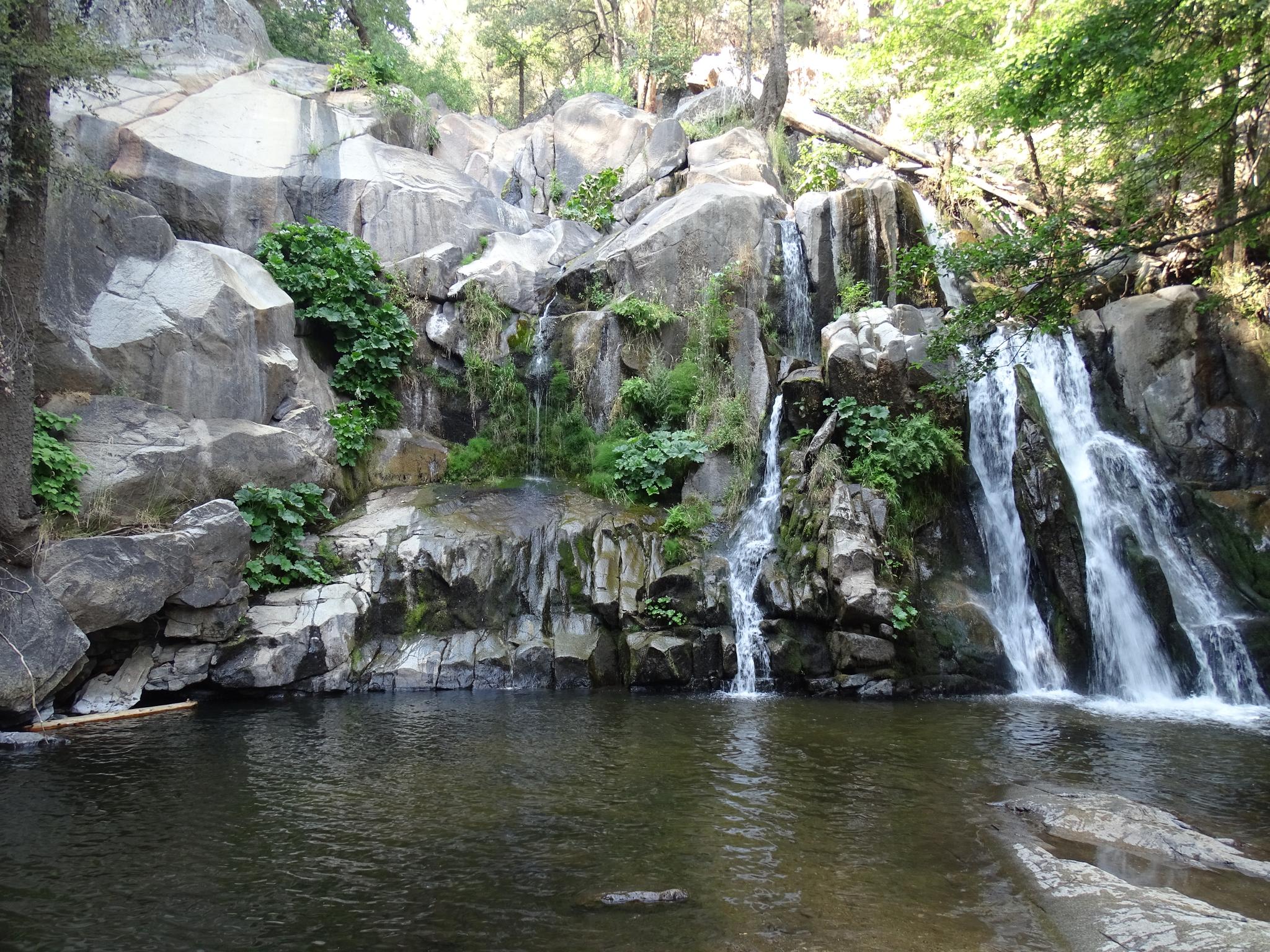 Multiple waterfalls tumble down large rocky cliffs into a dark pool.