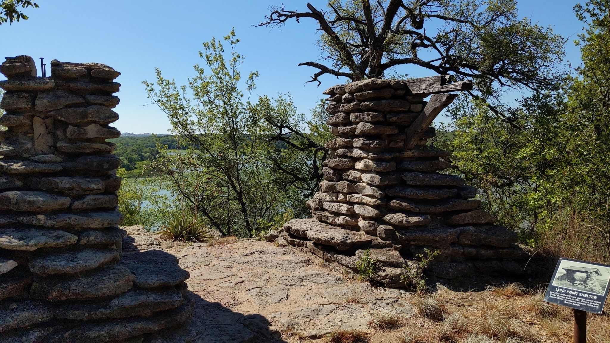 Two stacked stone structures overlook a sunny landscape with trees and water. - Trinity Trails: Fort Worth Nature Center Loop