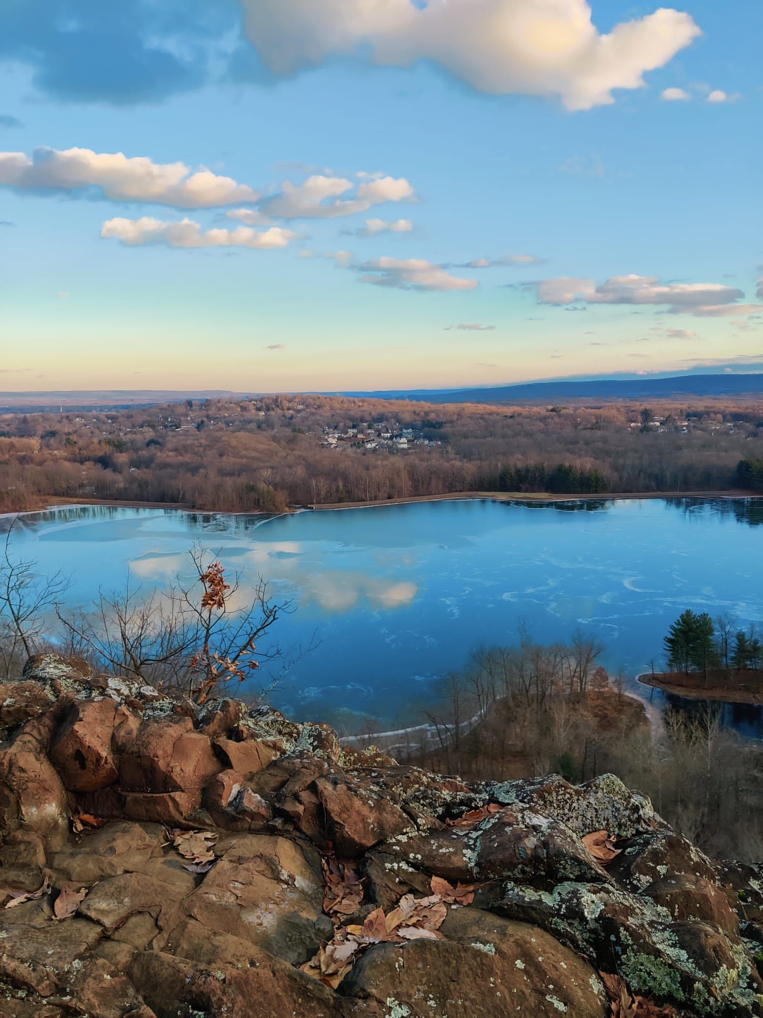Overlook of a partially frozen lake surrounded by bare trees under a cloudy sky. - Metacomet Trail Loop