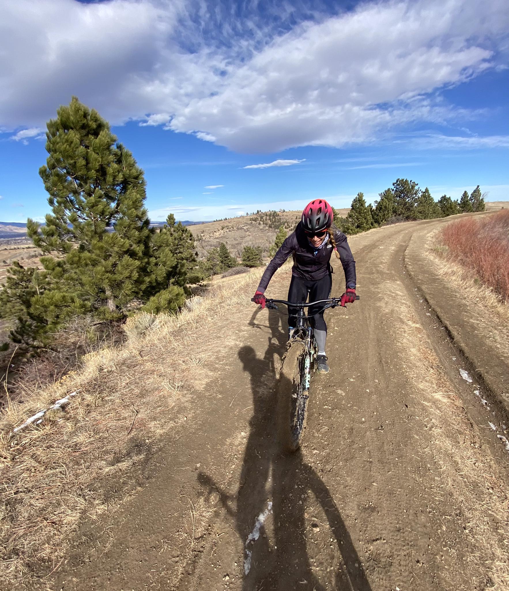 Mountain biker on a dirt trail under a partly cloudy sky.