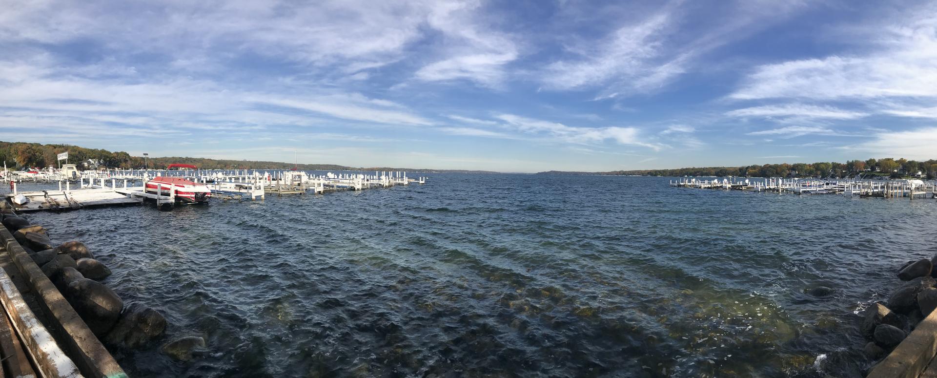 Panoramic view of a wide bay with boats docked on both sides under blue sky.