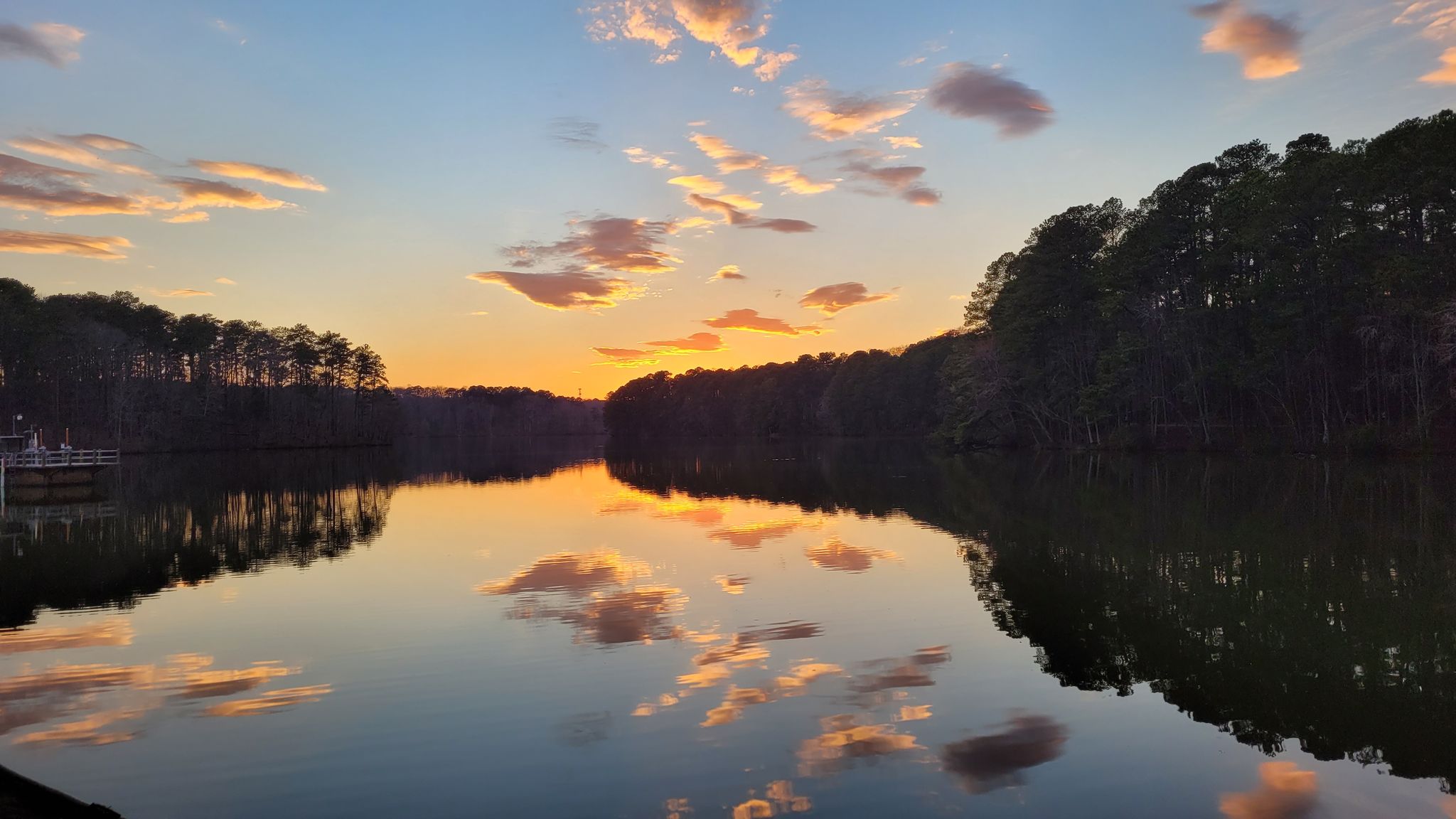 A lake reflecting a vibrant sunset with orange and pink clouds. - Lake Johnson Trail