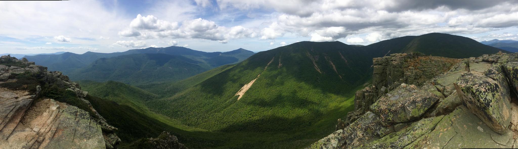 A panoramic view of vast green mountains and valleys under a partly cloudy sky.