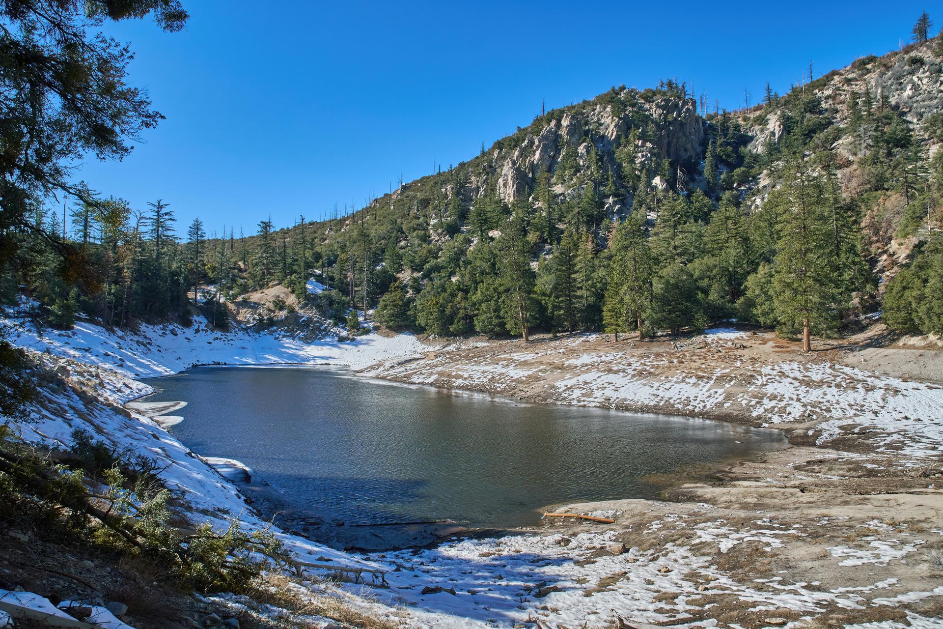 A serene lake surrounded by snow-covered banks and forested mountains.