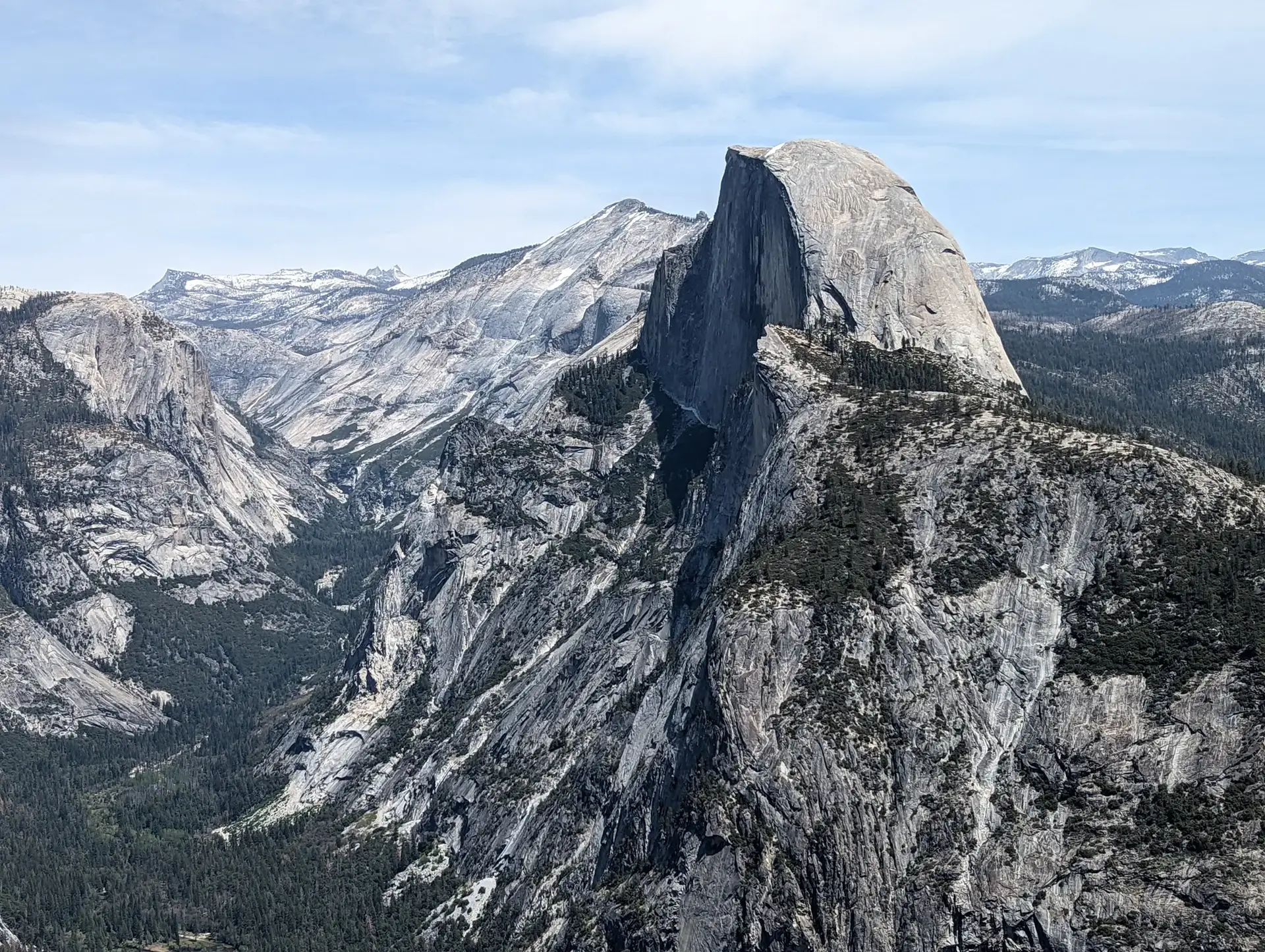 A massive granite dome rises above a vast, rugged mountain landscape.