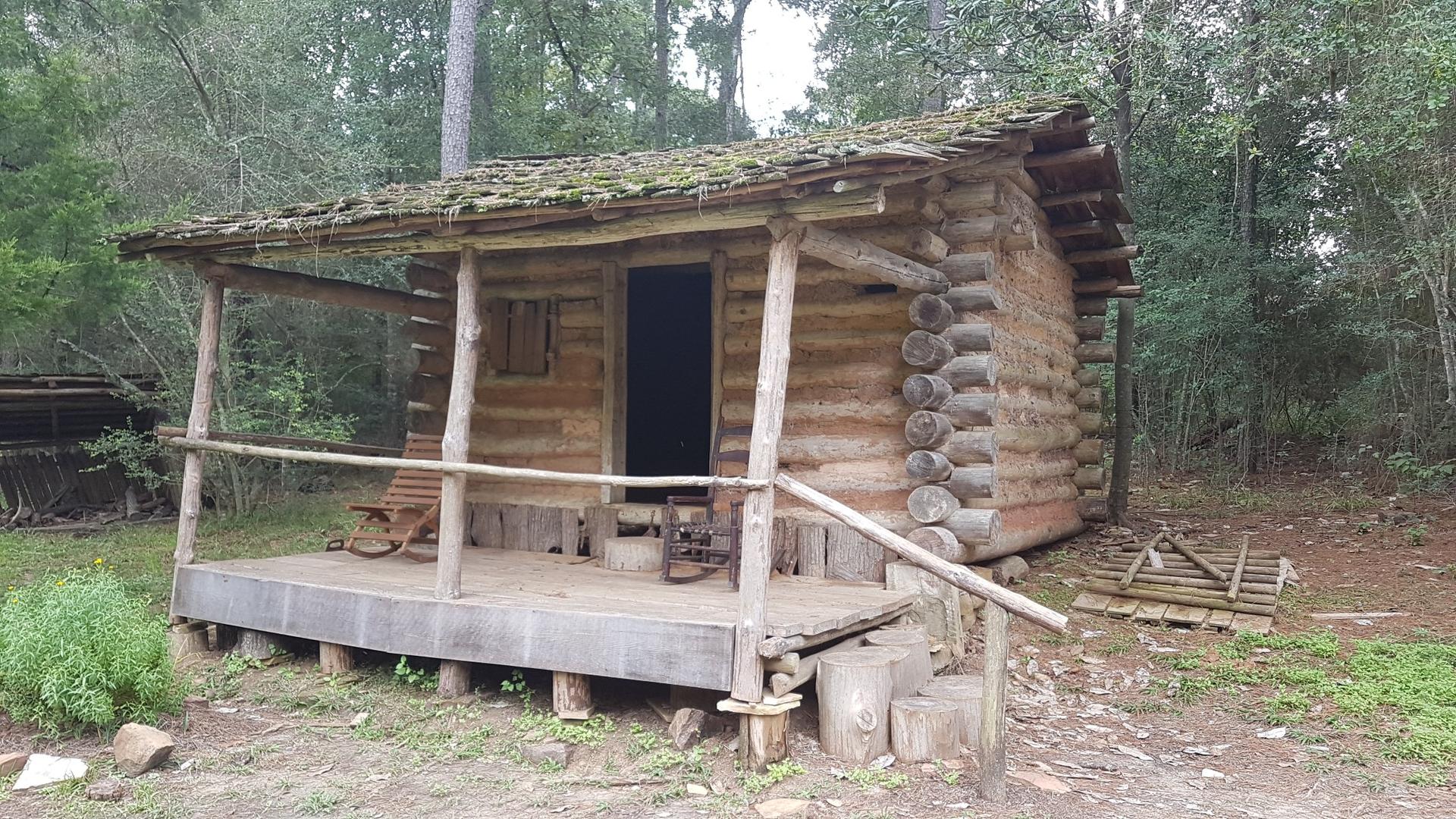 An old wooden log cabin with a porch and rocking chairs in a forest.