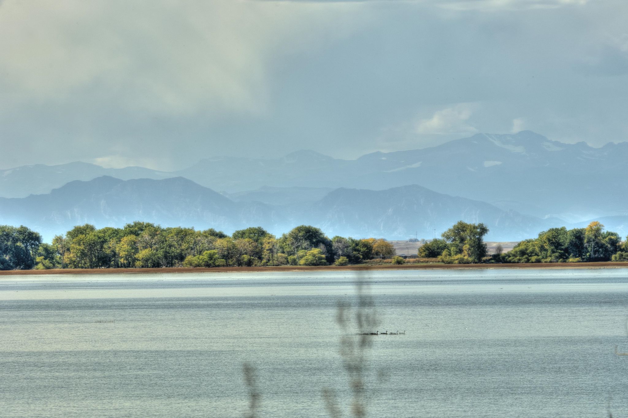 A serene lake with a forested shore and hazy mountains under an overcast sky. - Barr Lake Loop Trail