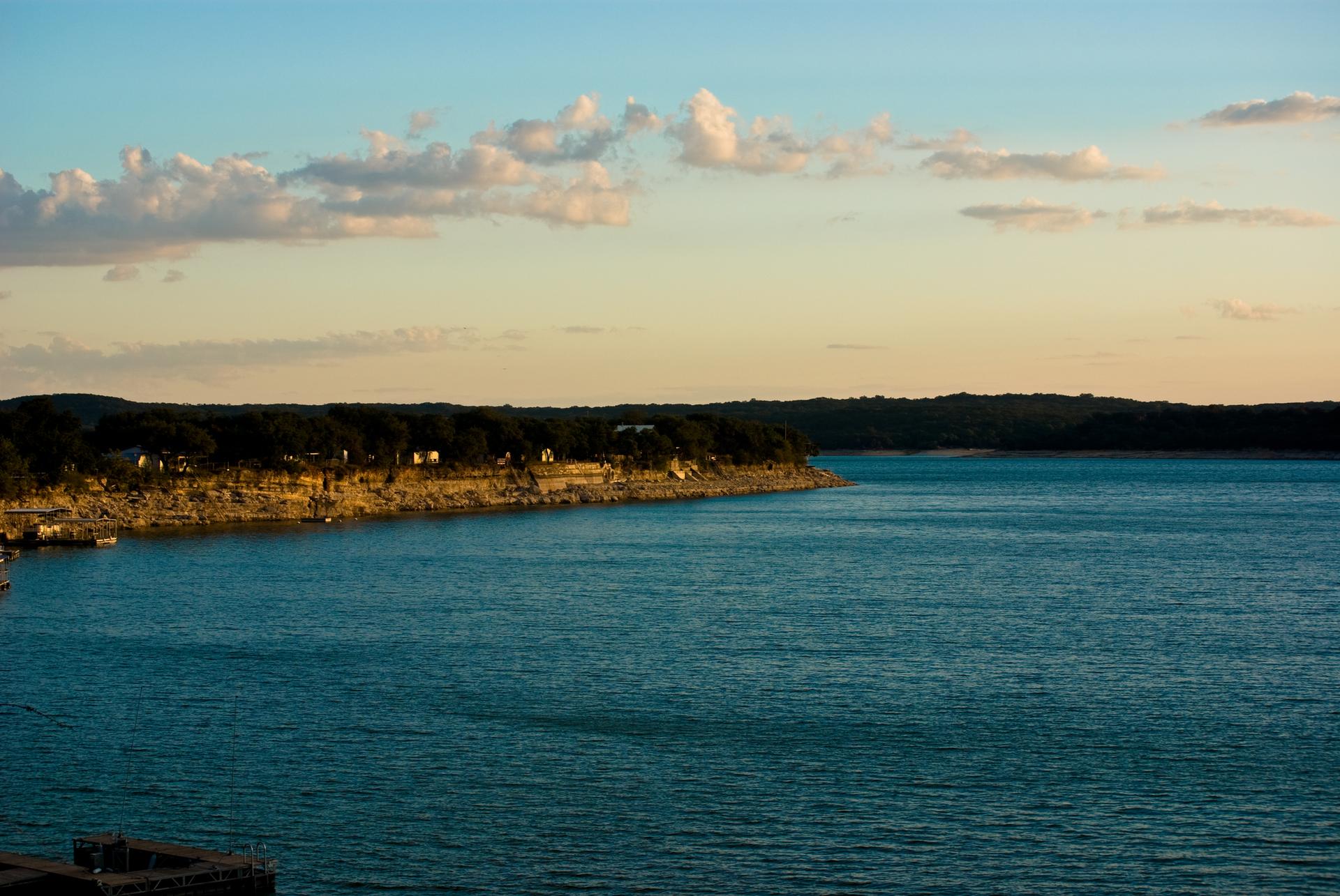Vast blue lake with a treed shoreline under a warm, cloudy sunset sky.