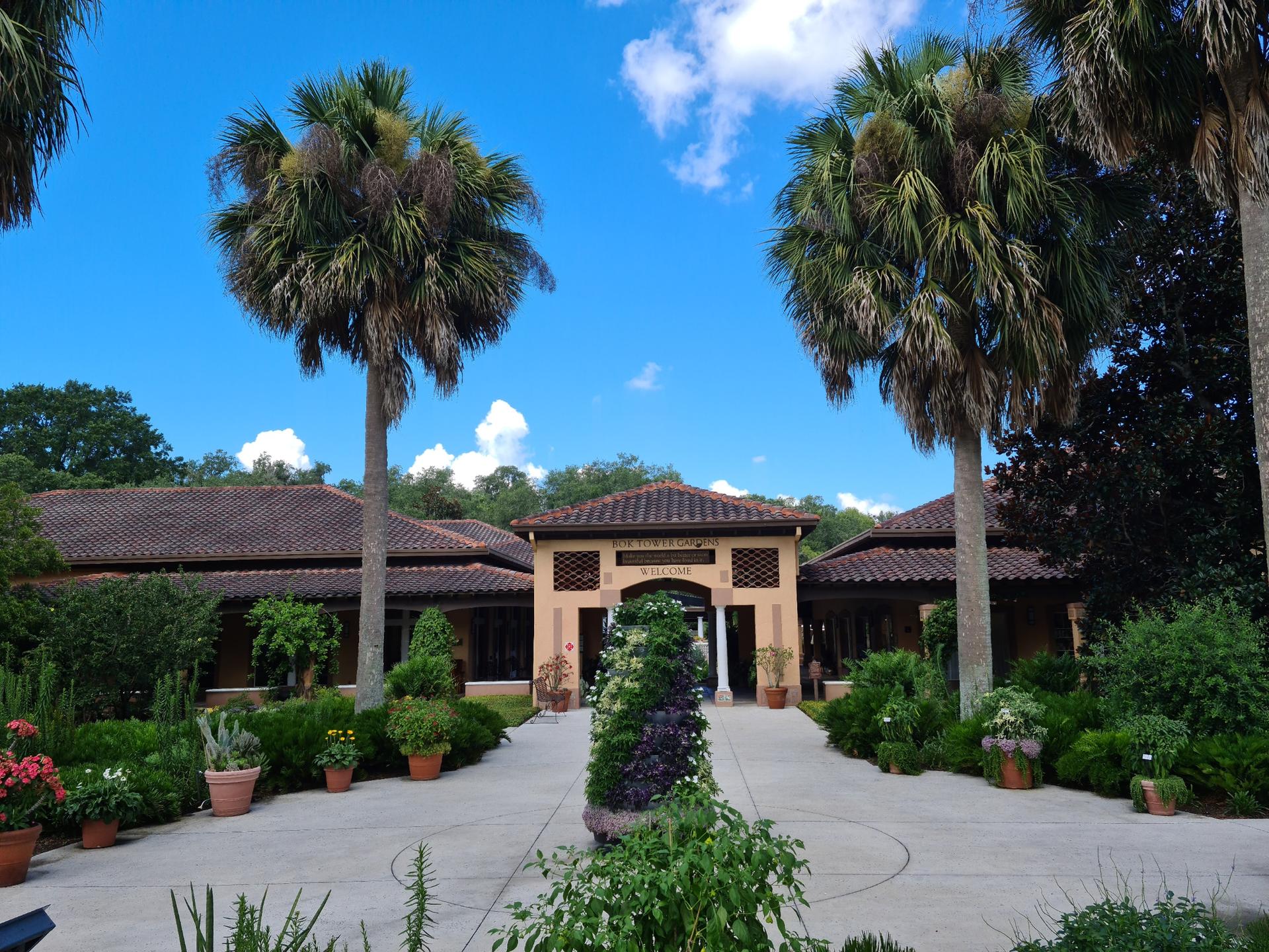 Building entrance with palm trees and manicured gardens under a bright sky.