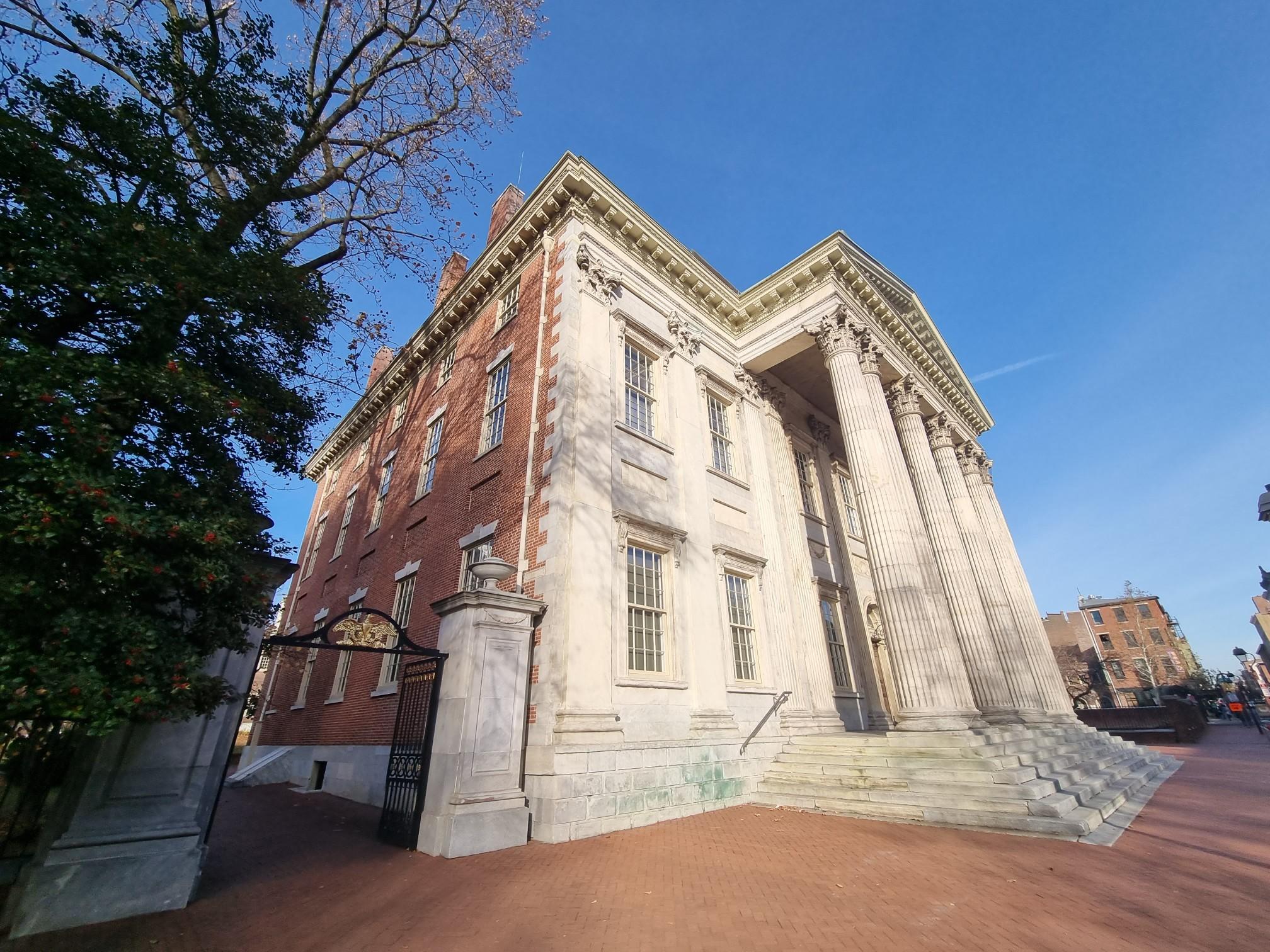 Grand historic building with large columns and brick facade under a bright blue sky.