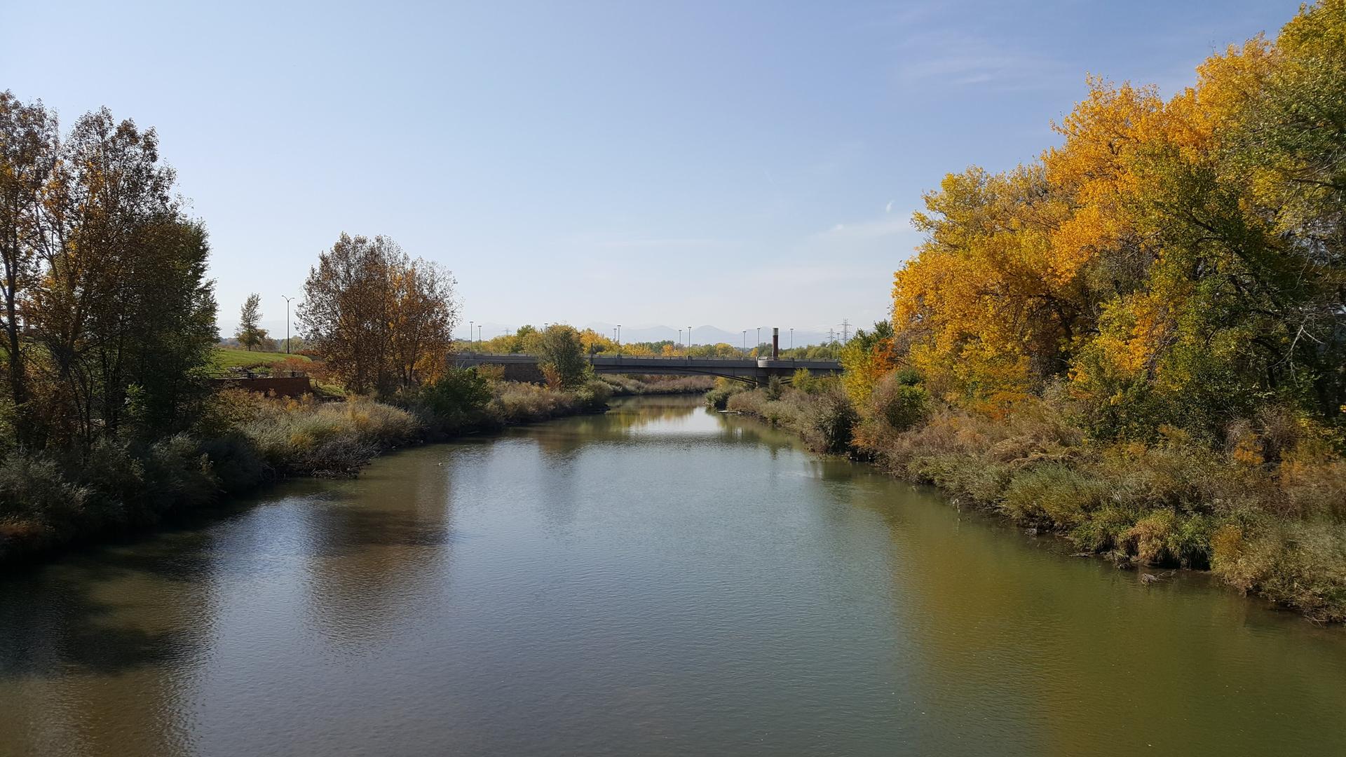 A river flowing between banks with vibrant autumn trees under a sunny sky.