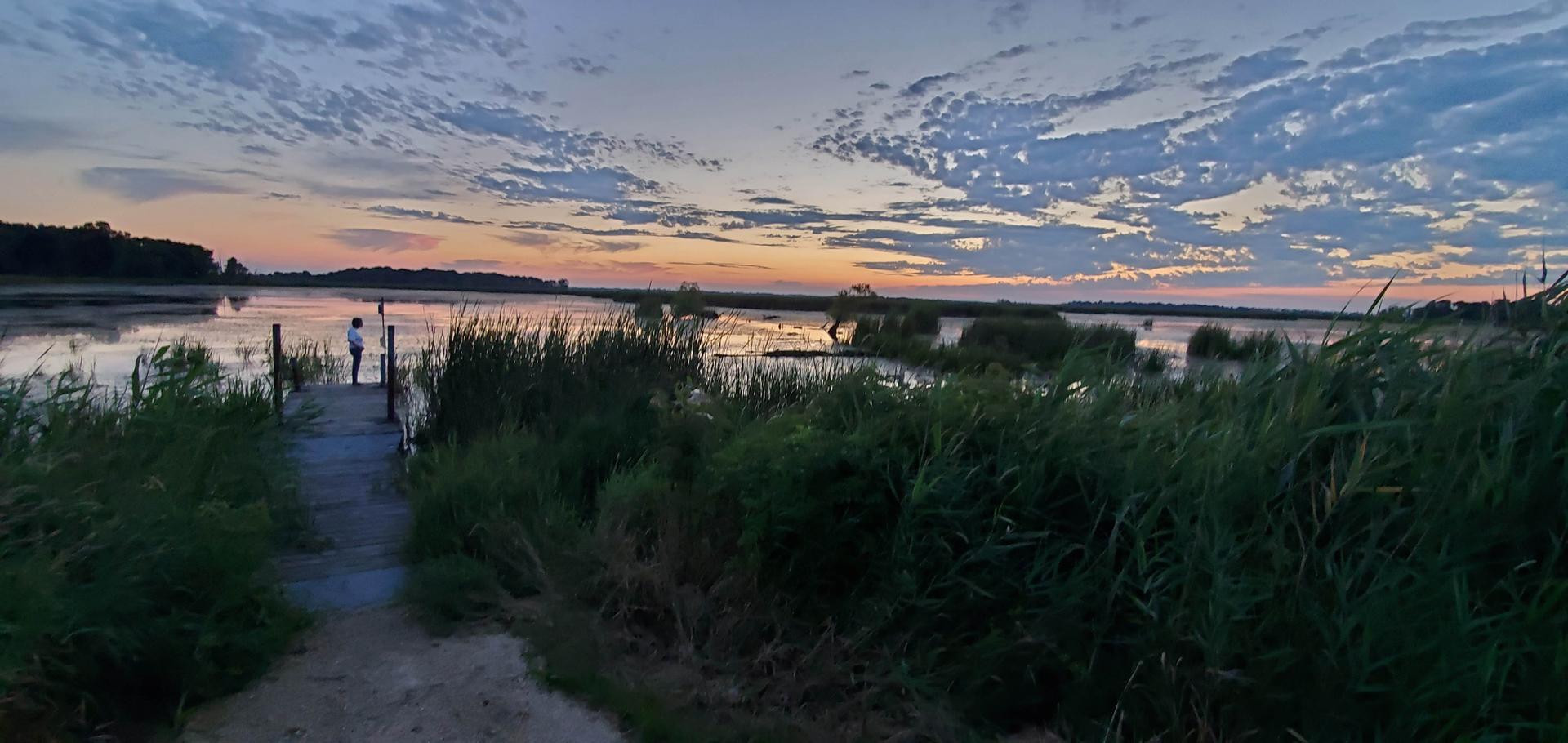 Two people on a dock at sunset over a marshy lake.