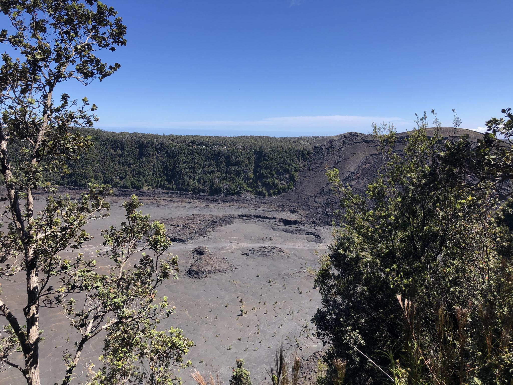 Overlook of a dark volcanic plain and distant forest under a clear blue sky.