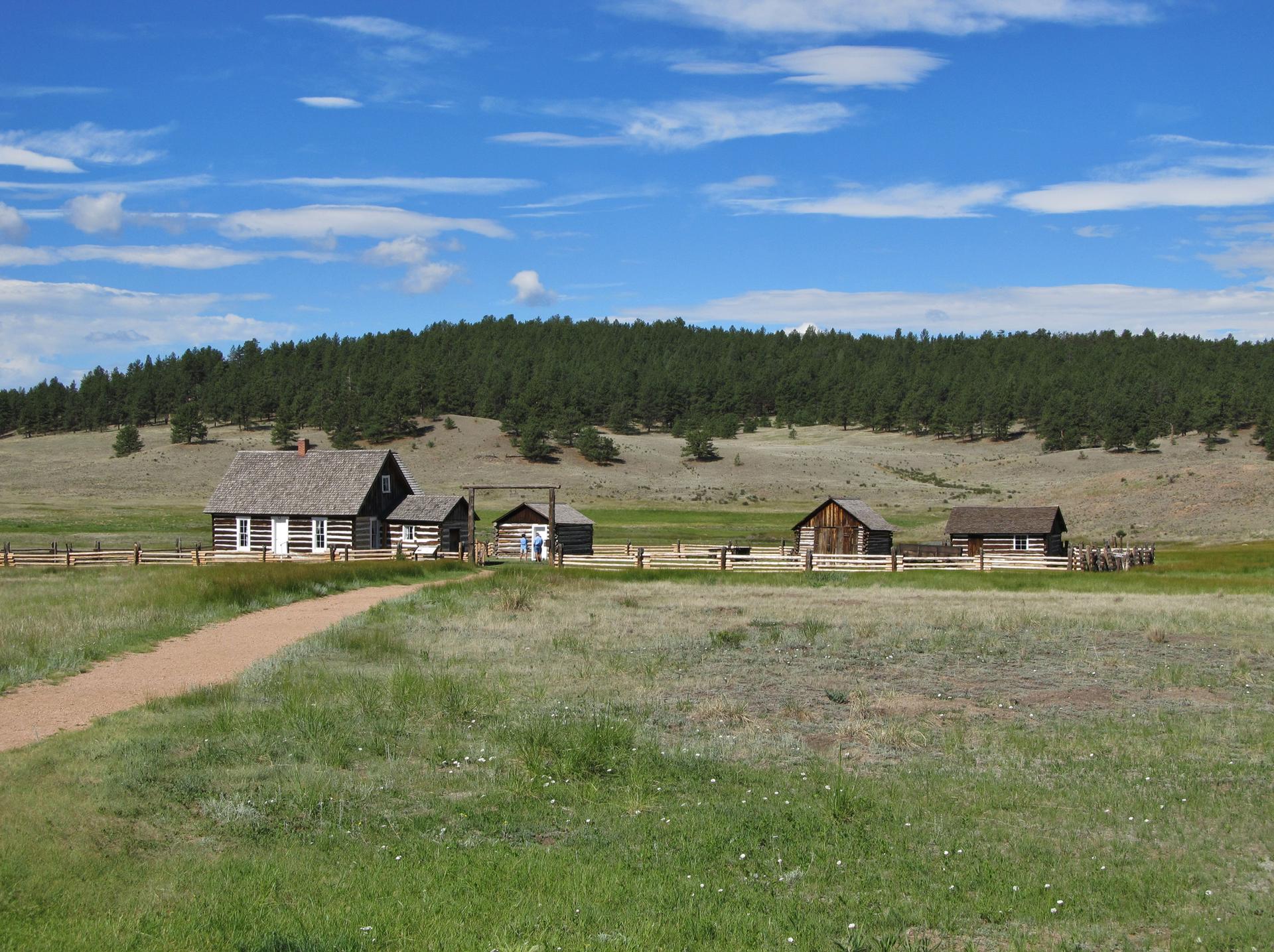 Historic wooden buildings in a green field under a bright, cloudy sky.