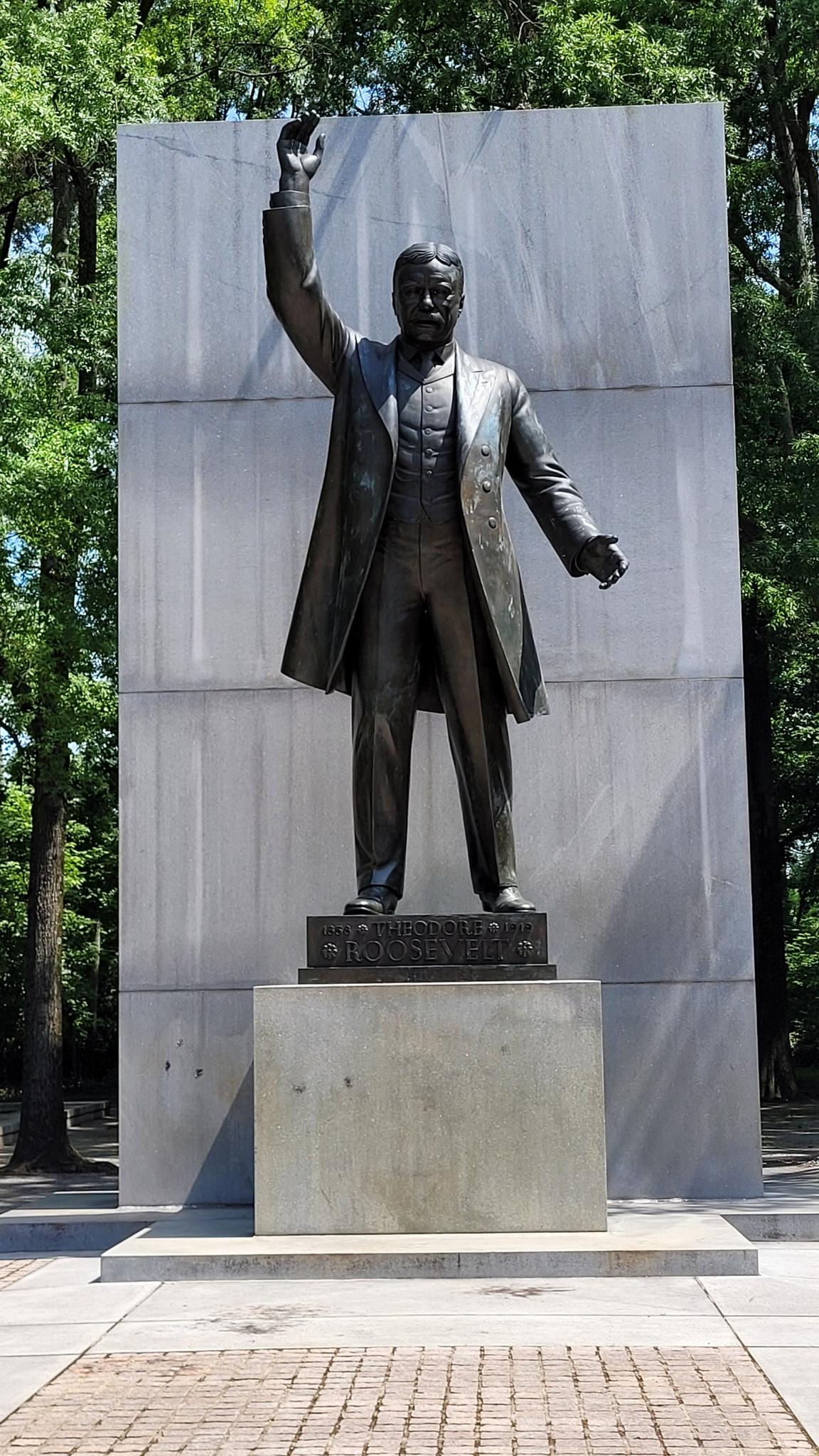 A bronze statue of a man with a raised arm against a stone wall.