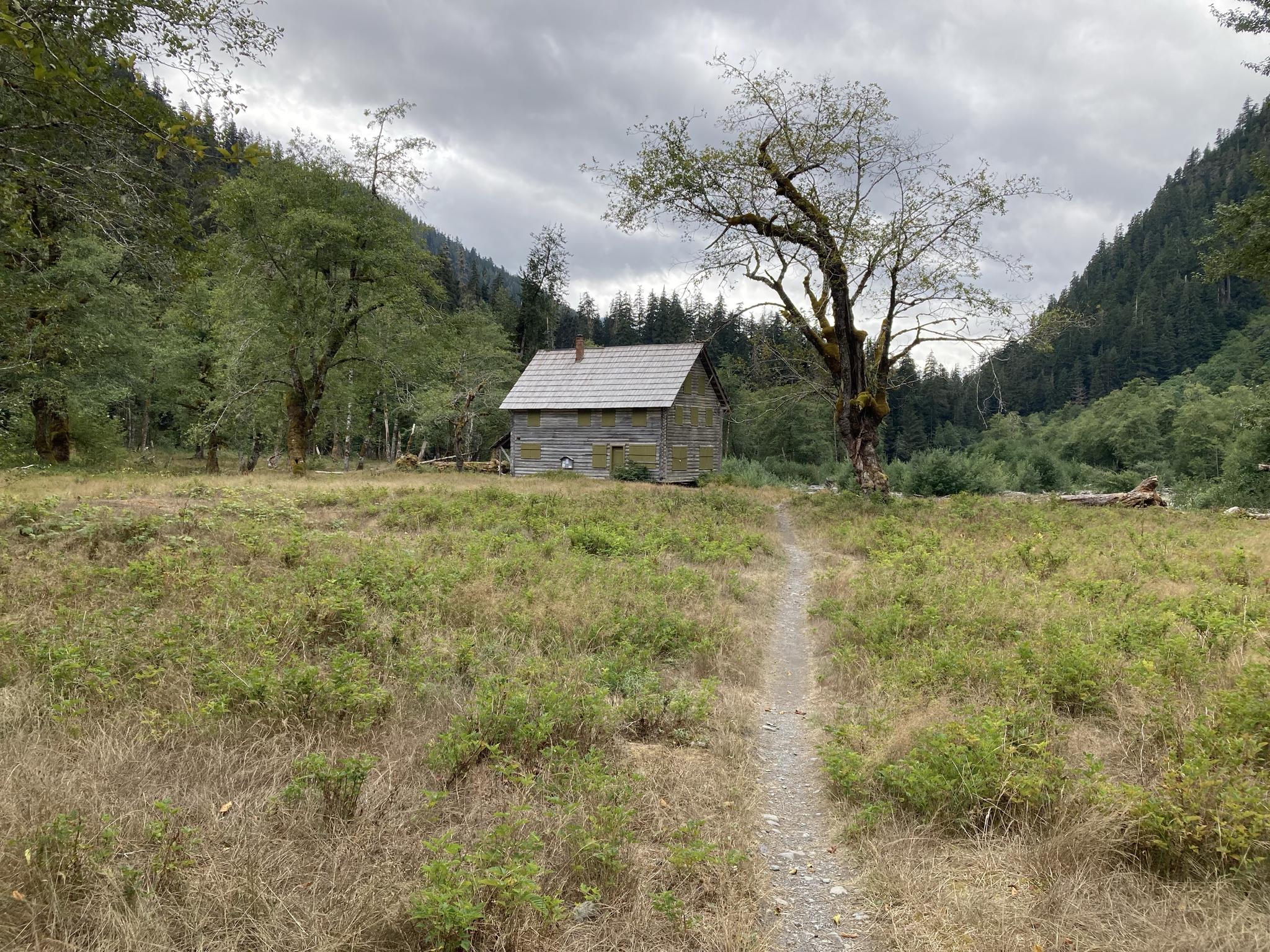 A small cabin sits in a grassy field with a path, under cloudy skies.