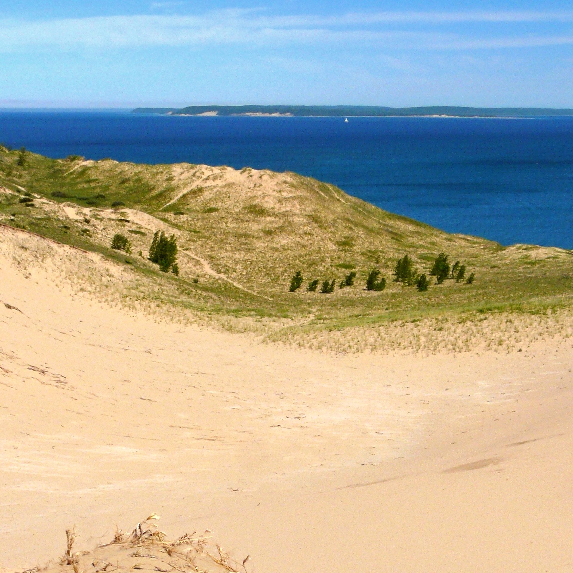 Vast sand dunes slope to a large blue body of water under a clear sky. - Glen Arbor – Sleeping Bear Dunes loop from Glen Lake Ridgeline