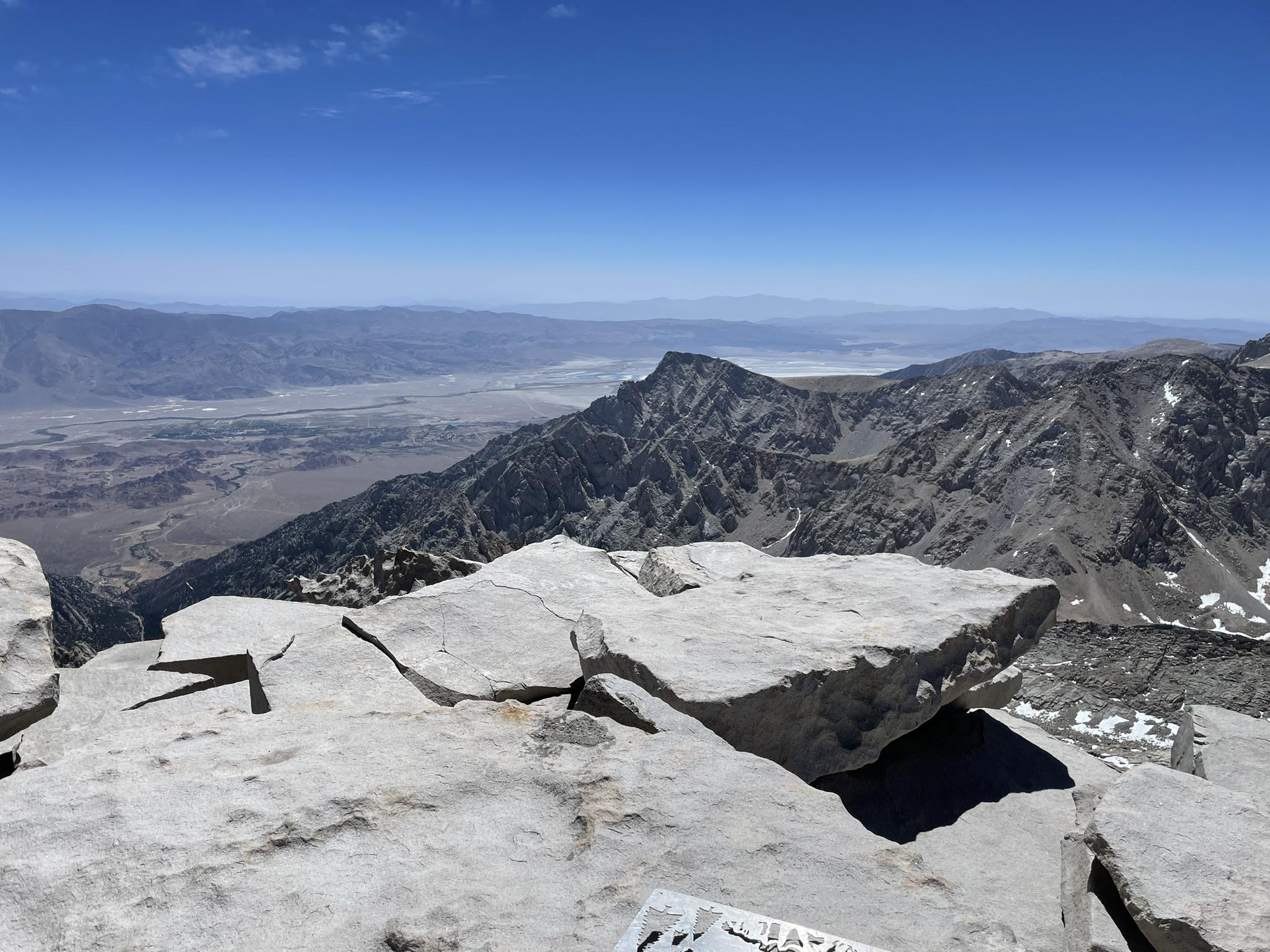 Rocky mountain peak with vast valley and distant mountains under a clear sky.