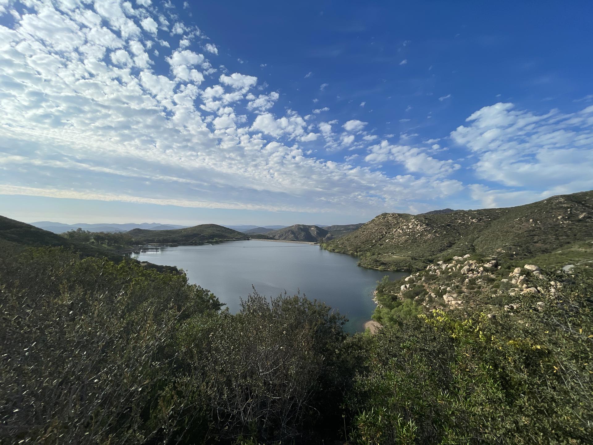 Expansive lake surrounded by green mountains under a bright, cloudy sky.