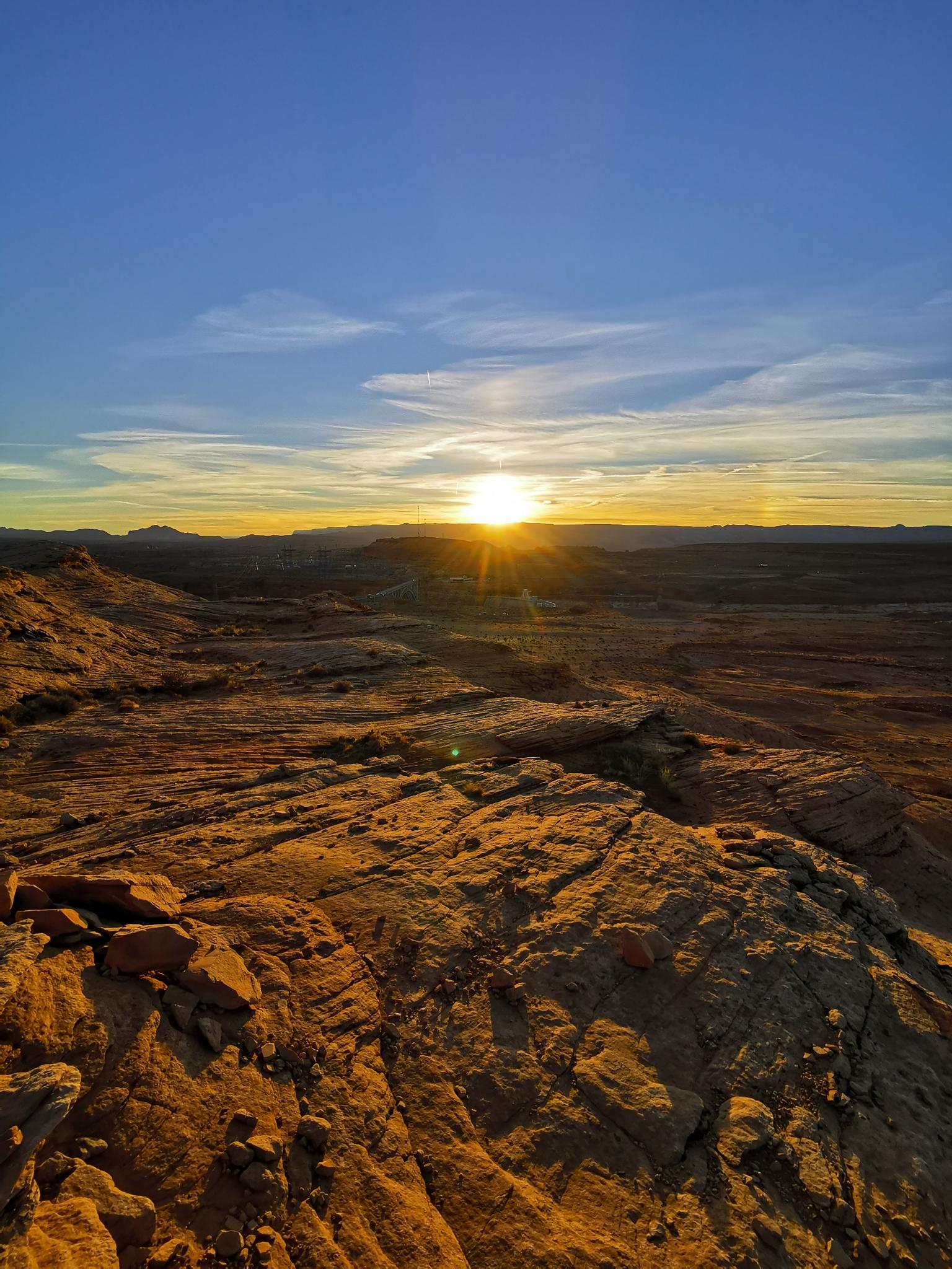 Golden sunset over rugged, rocky desert landscape under a blue sky.