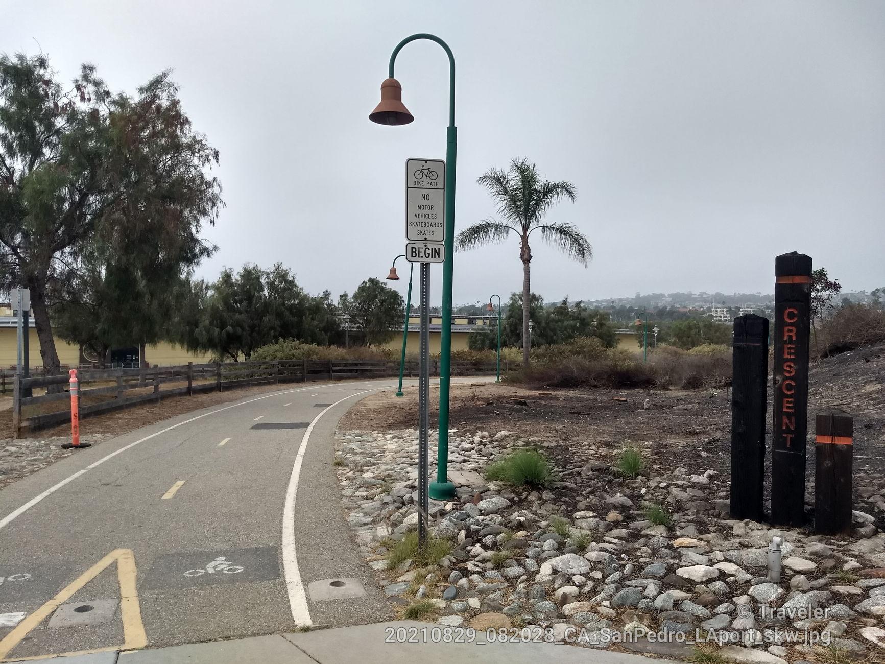Paved path with a street lamp and signs under an overcast sky.
