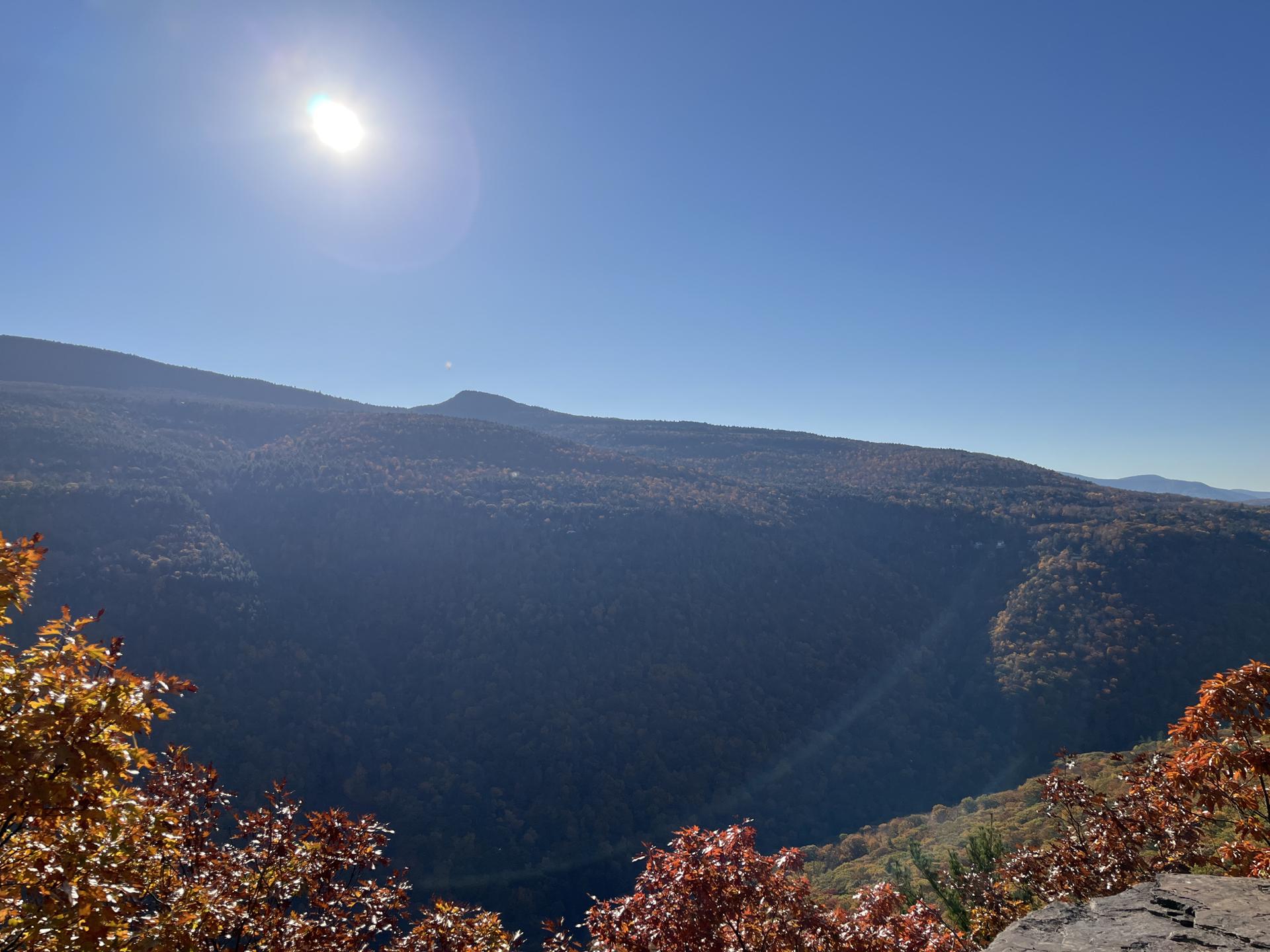A sunny mountain valley with autumn trees and a bright sun in a clear sky.