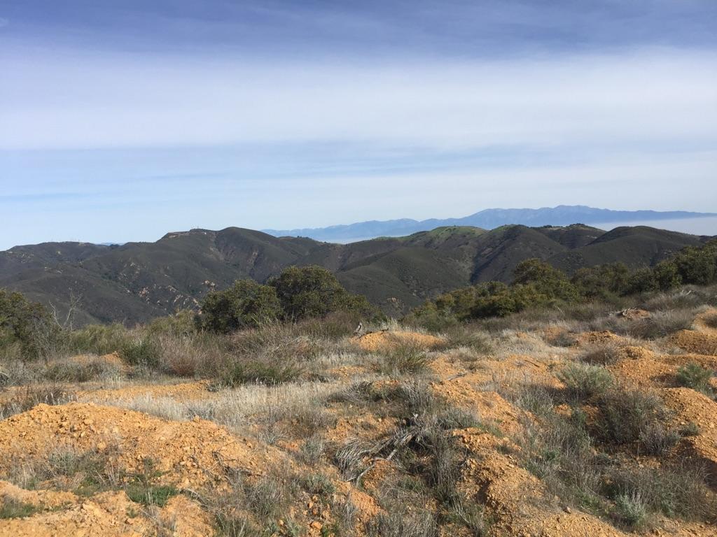 Dry, rocky foreground with distant green mountains under a hazy blue sky.