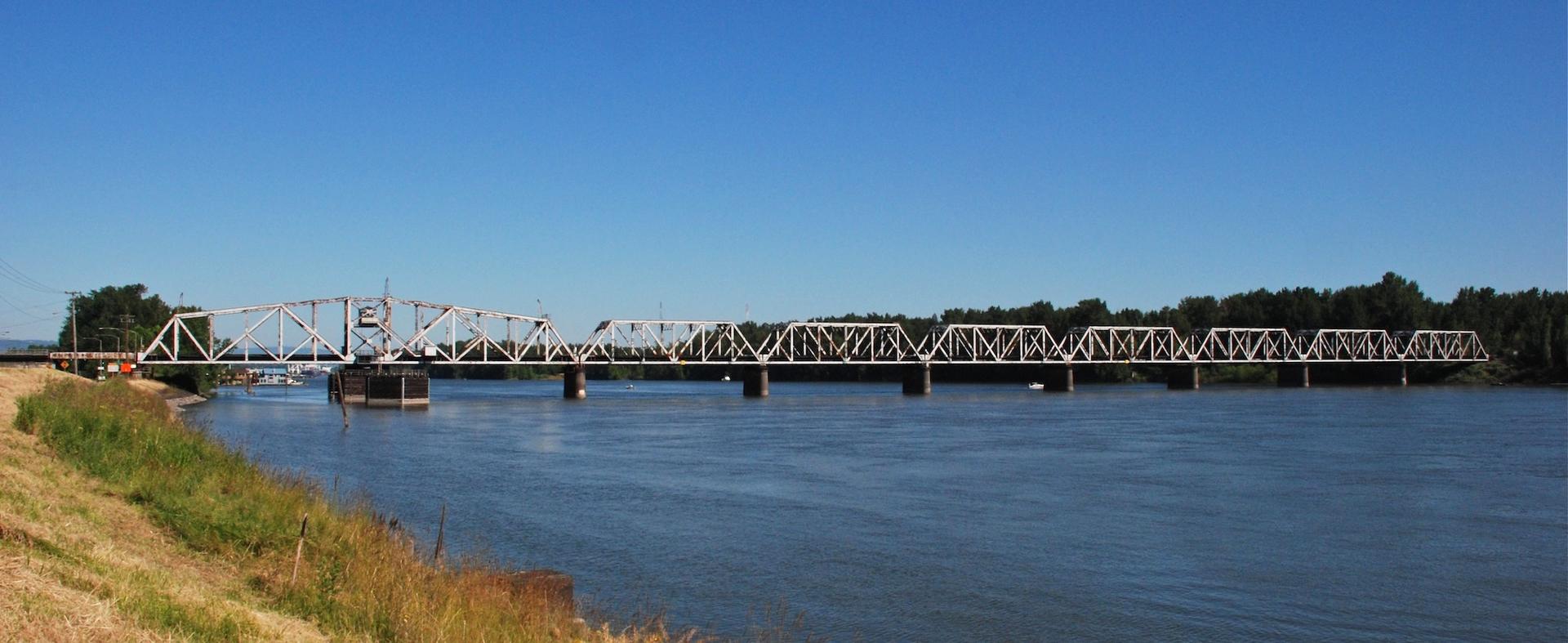 Long metal truss bridge spanning a wide river under a clear blue sky.