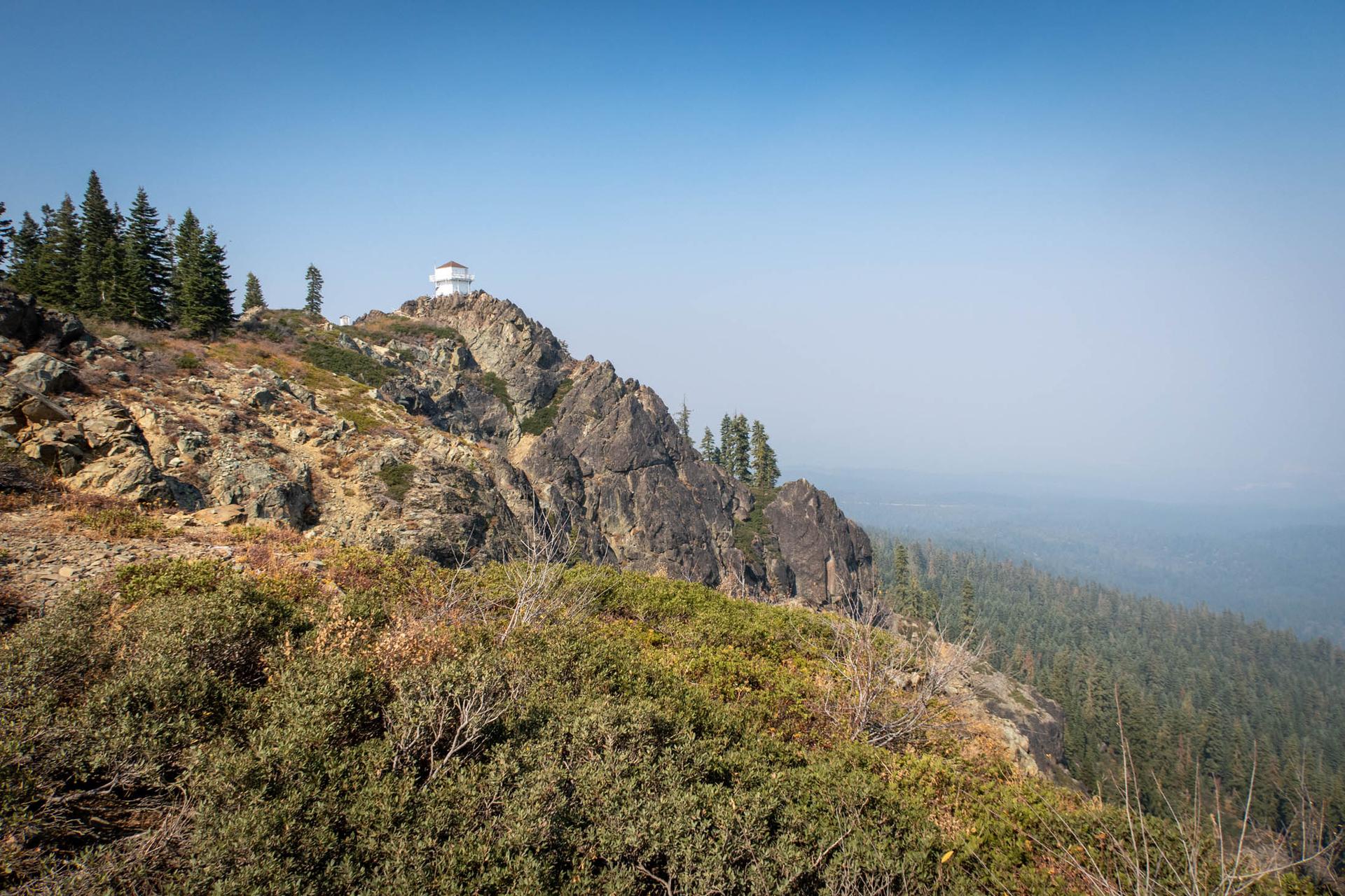 A white building atop a rocky mountain peak overlooking a hazy valley.