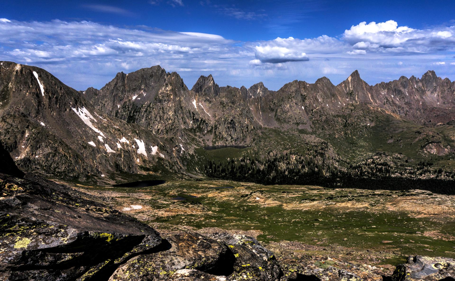Rugged mountain range with jagged peaks, snow patches, and green valleys.