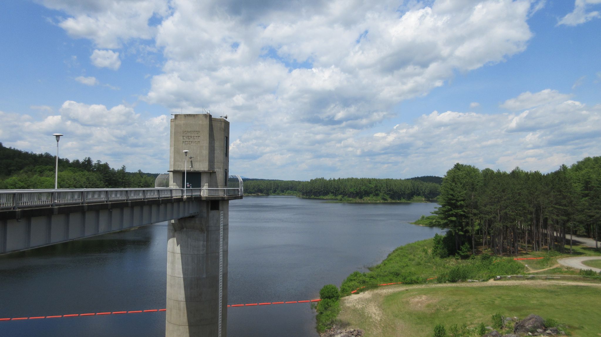 Concrete bridge and tower span a wide lake under a bright, cloudy sky. - Goffstown Rail Trail and Everett Lake Loop