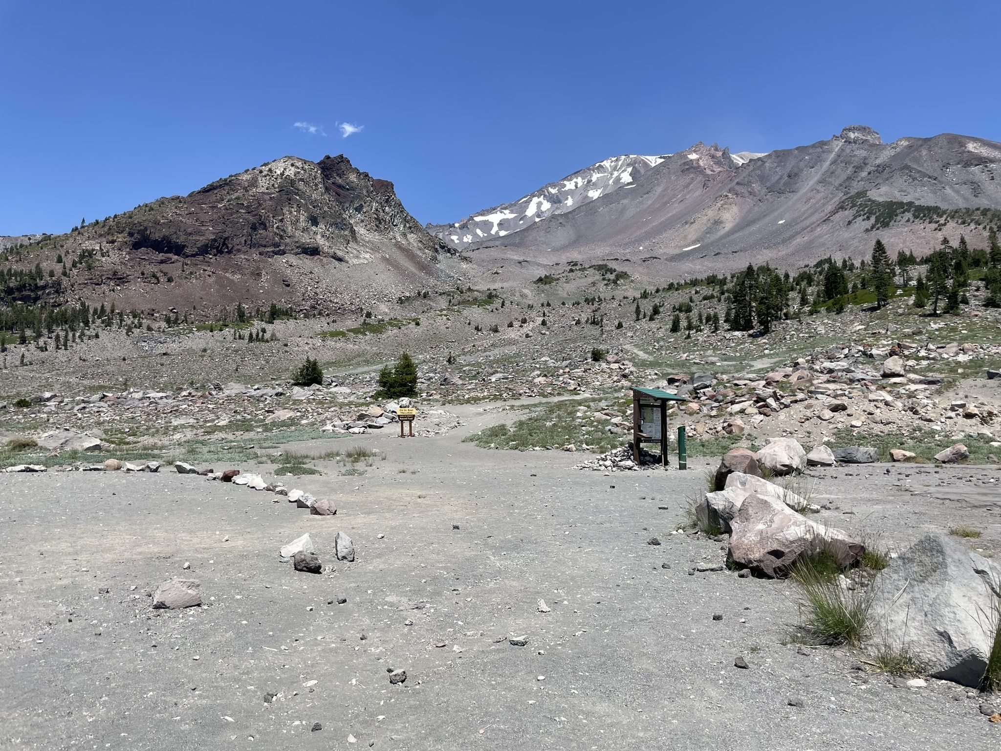 Rocky mountain landscape under clear sky, distant snow, person near trail sign. - South Gate Meadows Trail